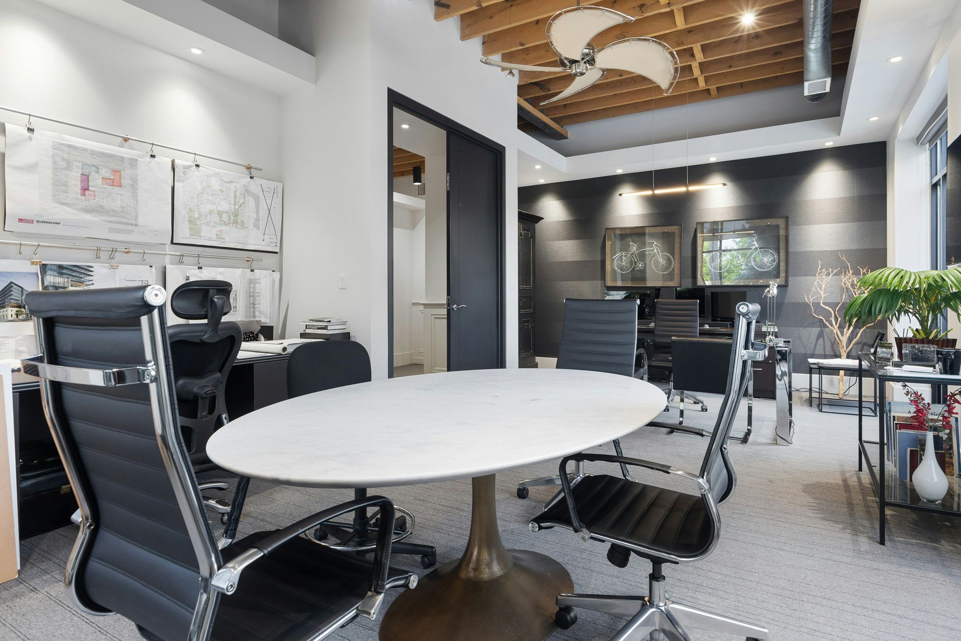 Office with round table, black chairs, drawings on wall, and a black door.
