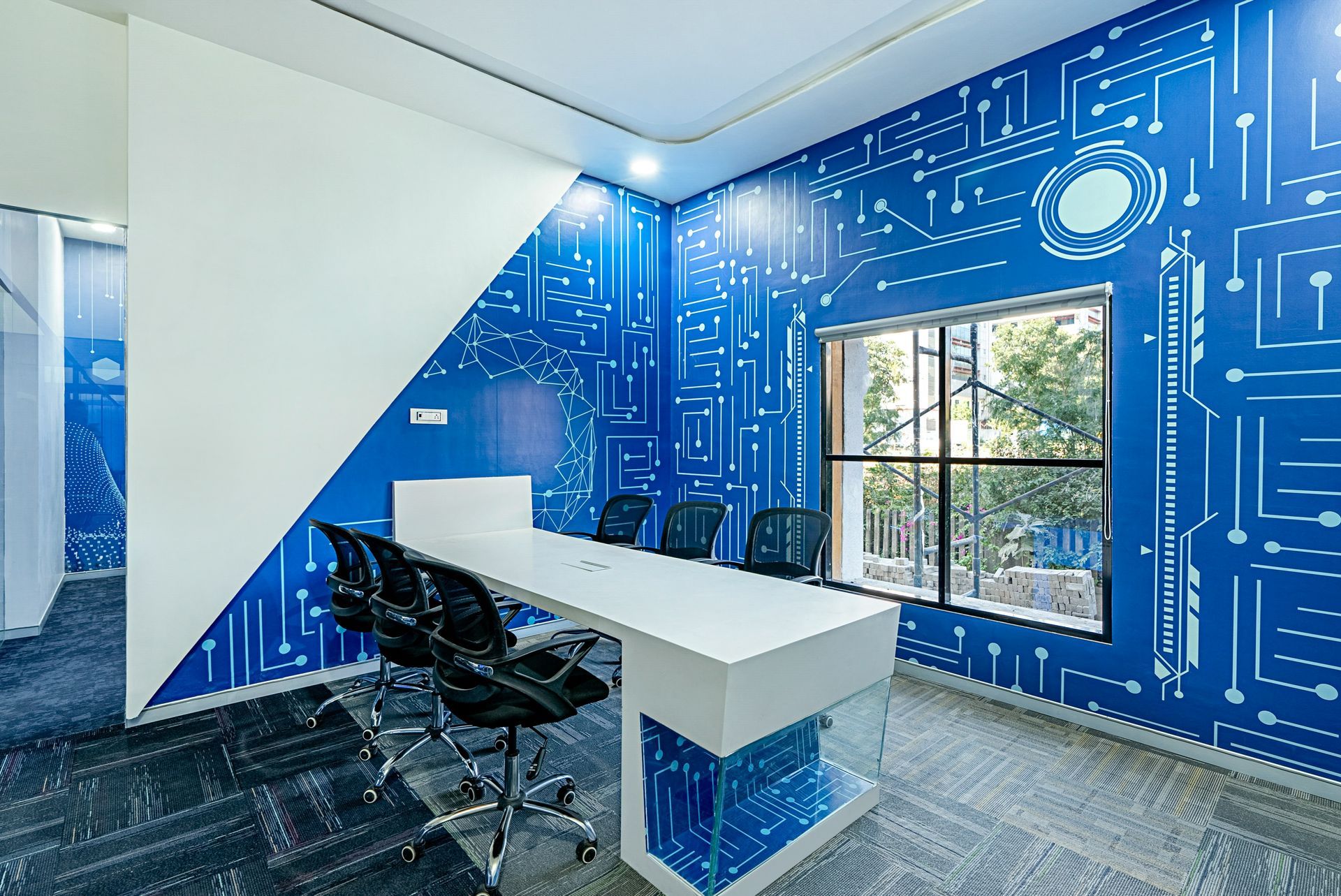 Blue-walled office with circuit board design, white desk, black chairs, window to outside.