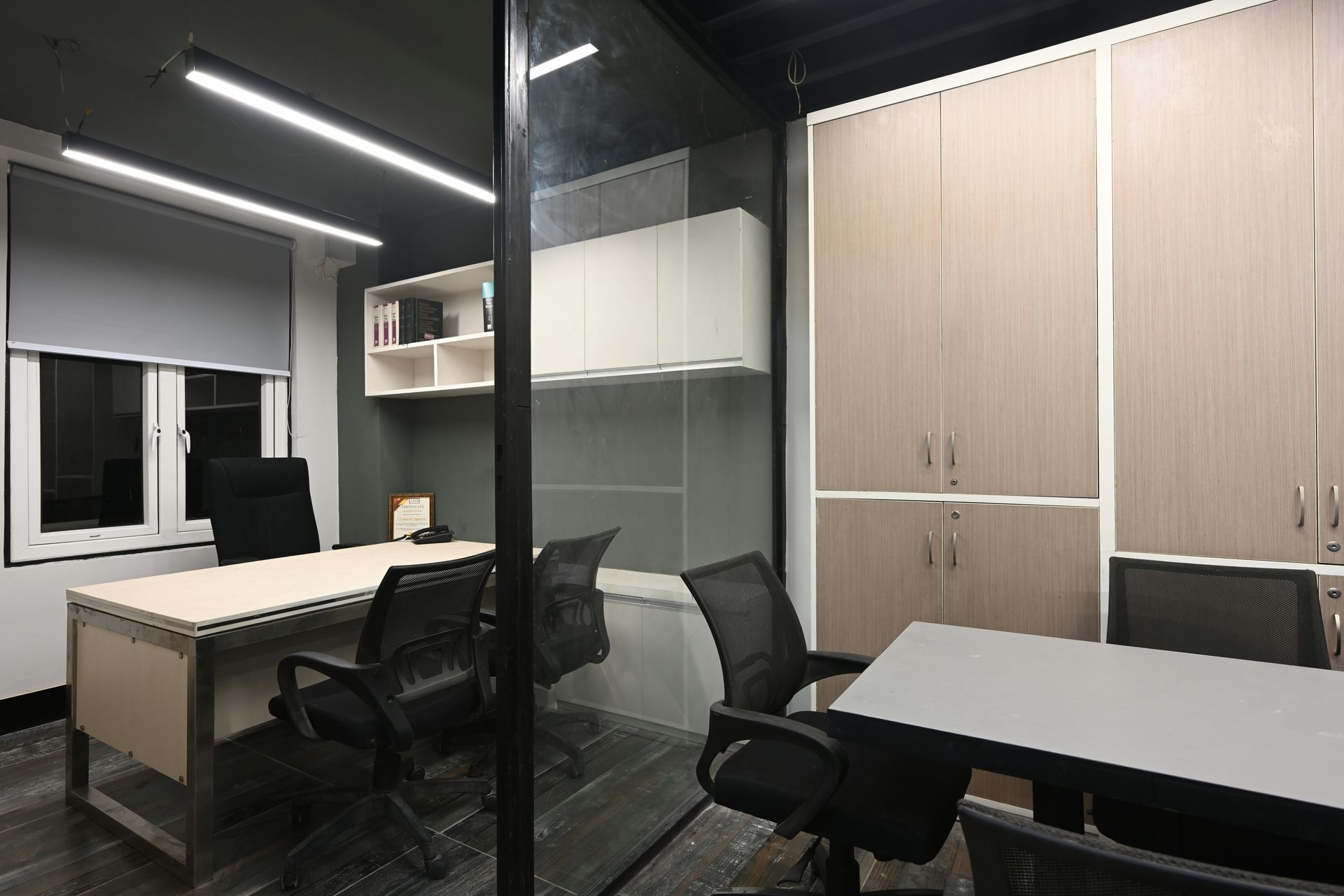 Office interior with desks, chairs, cabinets, glass partition, window, and overhead lighting.