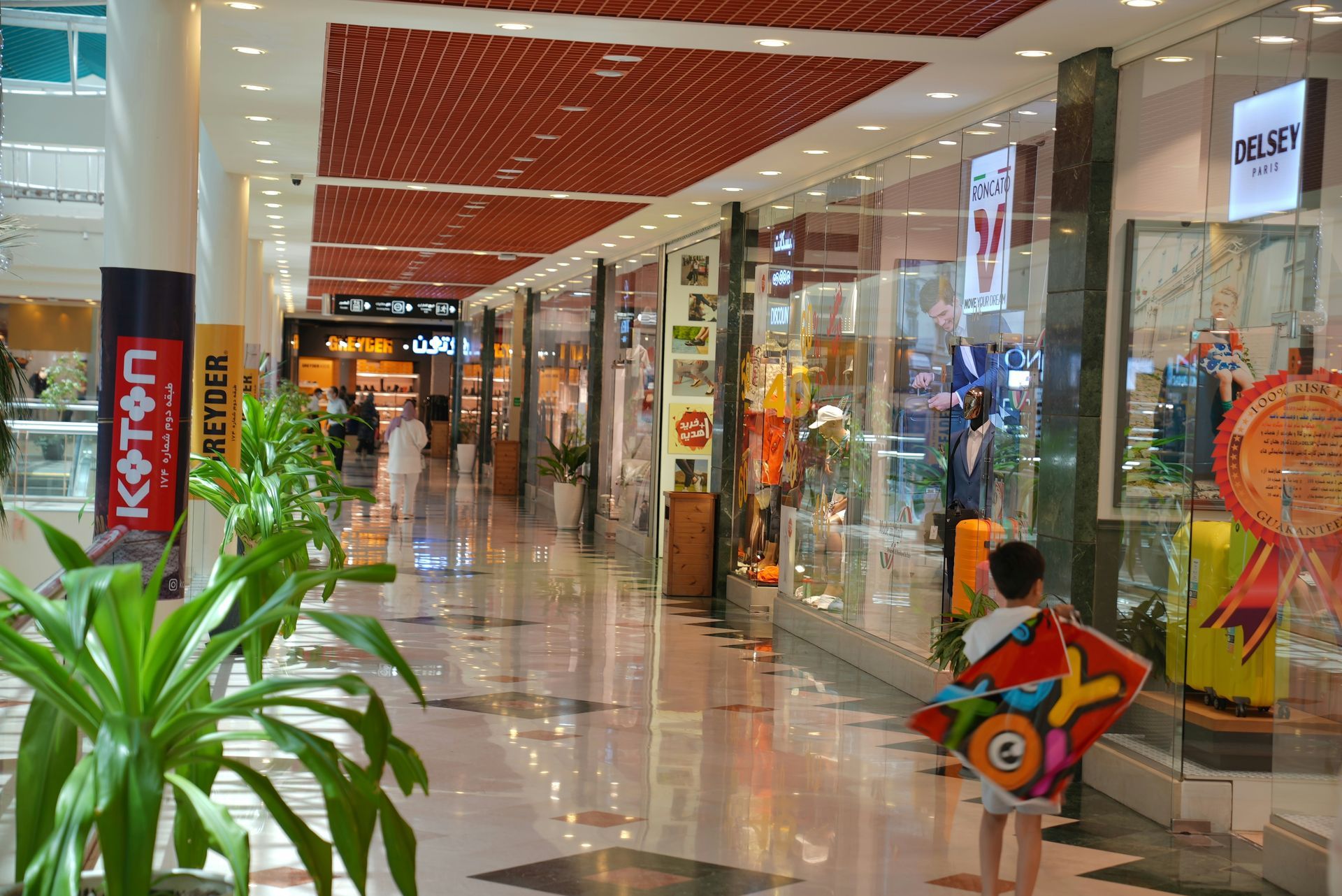 Mall interior with shops, red ceiling, and a child holding a kite.
