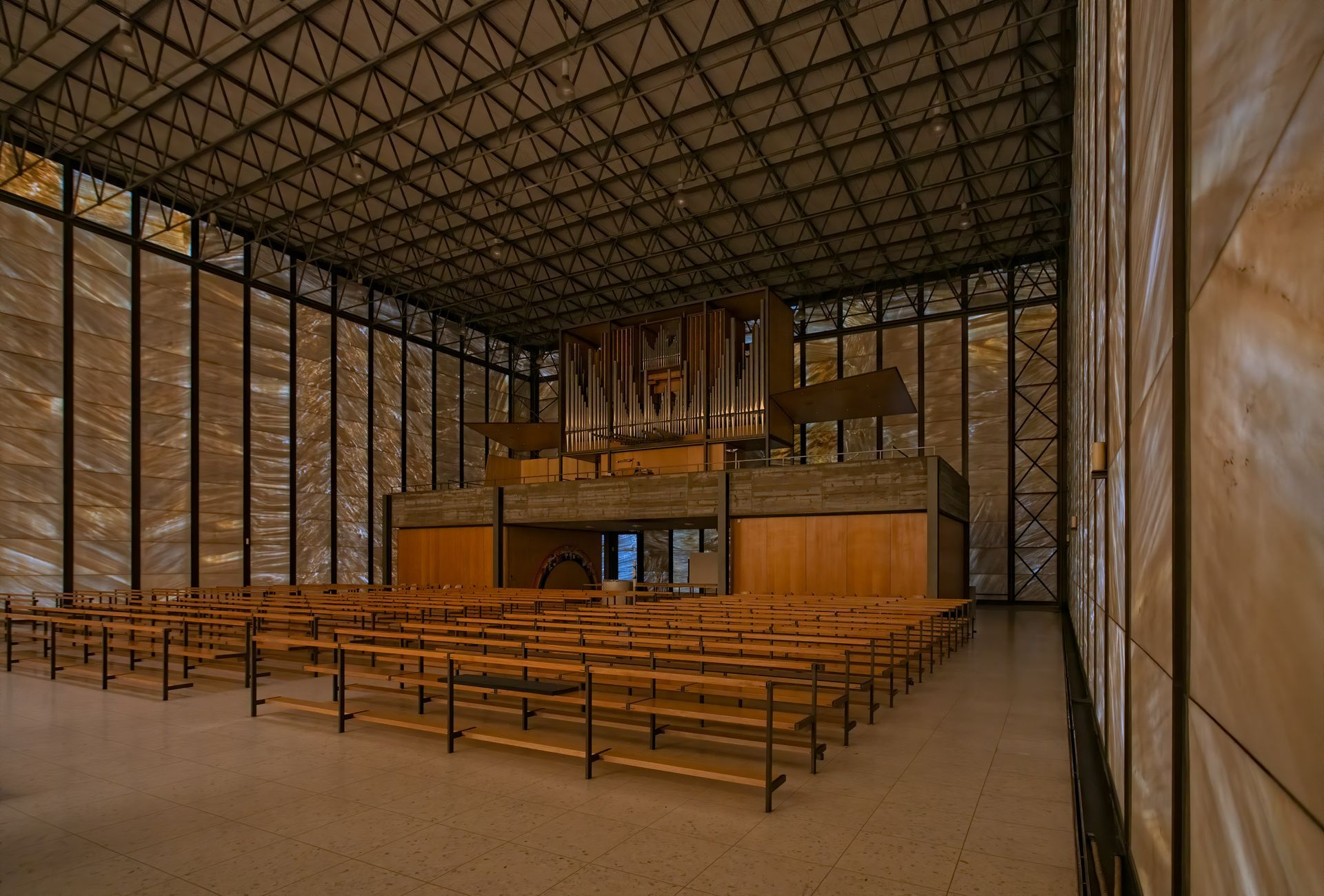 Church interior with wooden pews facing a large pipe organ on a raised platform. Tall windows let in light.