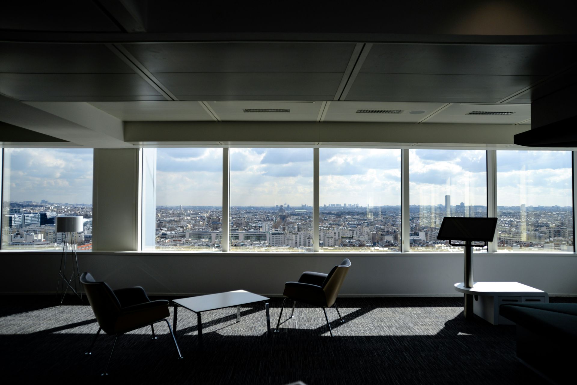 Office lounge with cityscape view through large windows. Two chairs and a table sit in front of the glass.