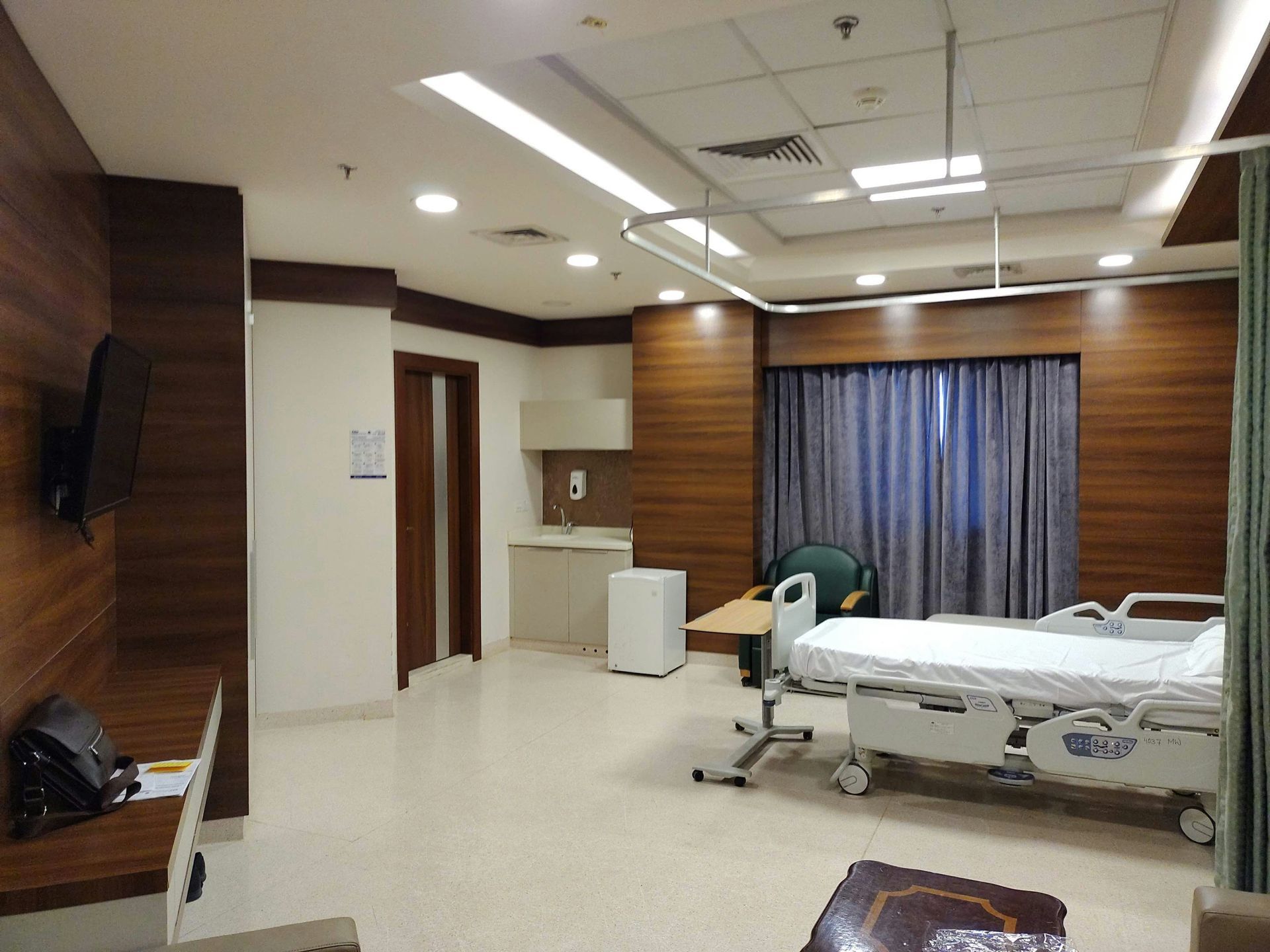 Hospital room with bed, desk, and wood paneling.