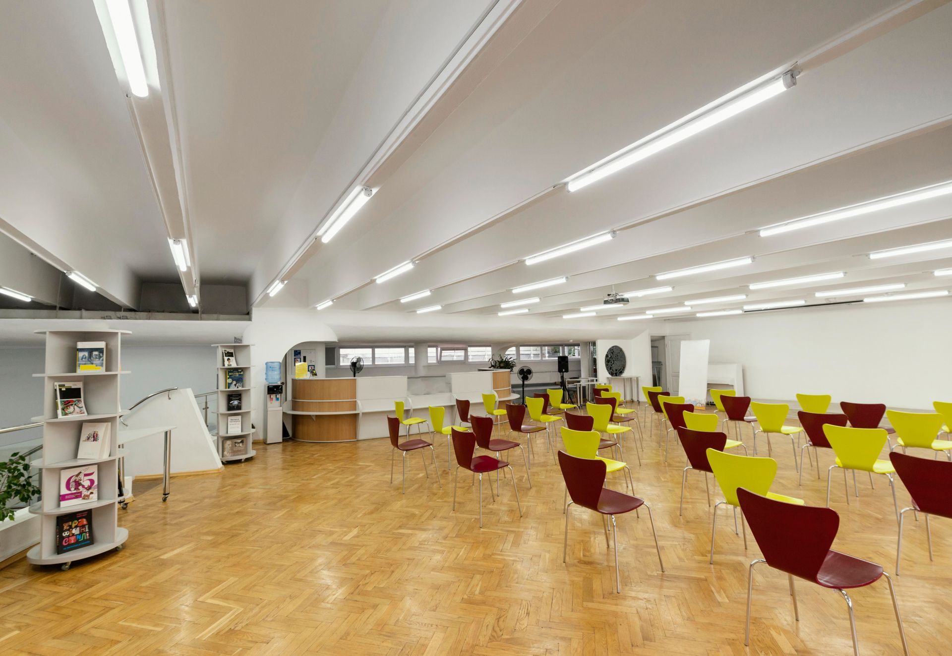 An empty event space with rows of red and yellow chairs, light-colored wood floors, and a reception area.