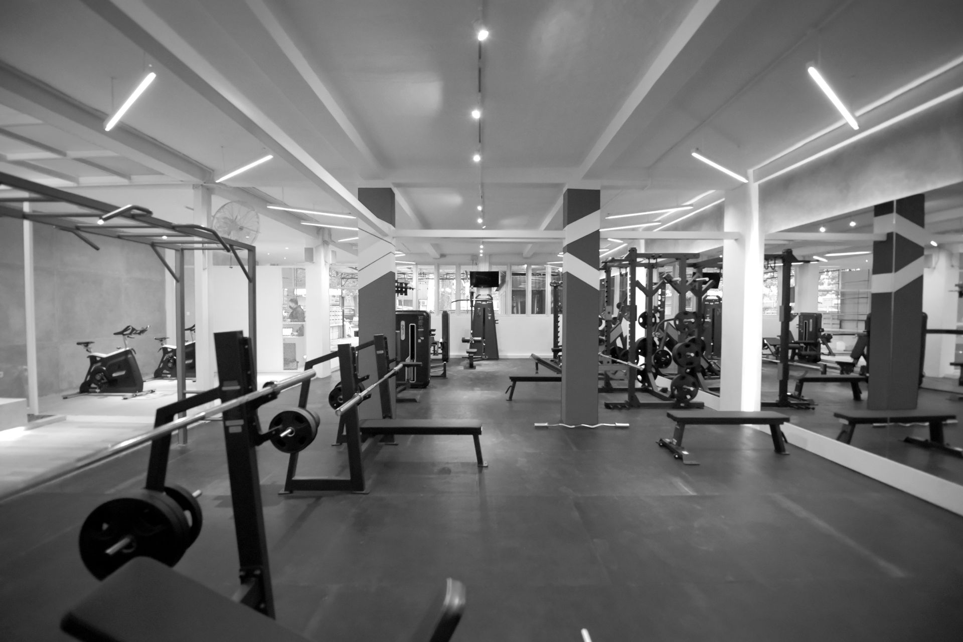 A grayscale view of a gym interior with weight benches, equipment, and mirrors.