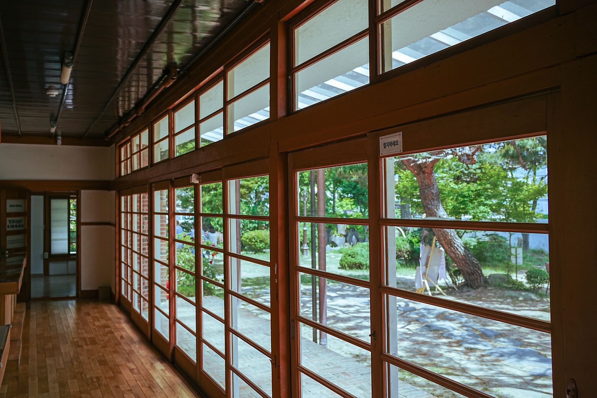 Wooden-framed windows lining a room, overlooking a sunny garden.