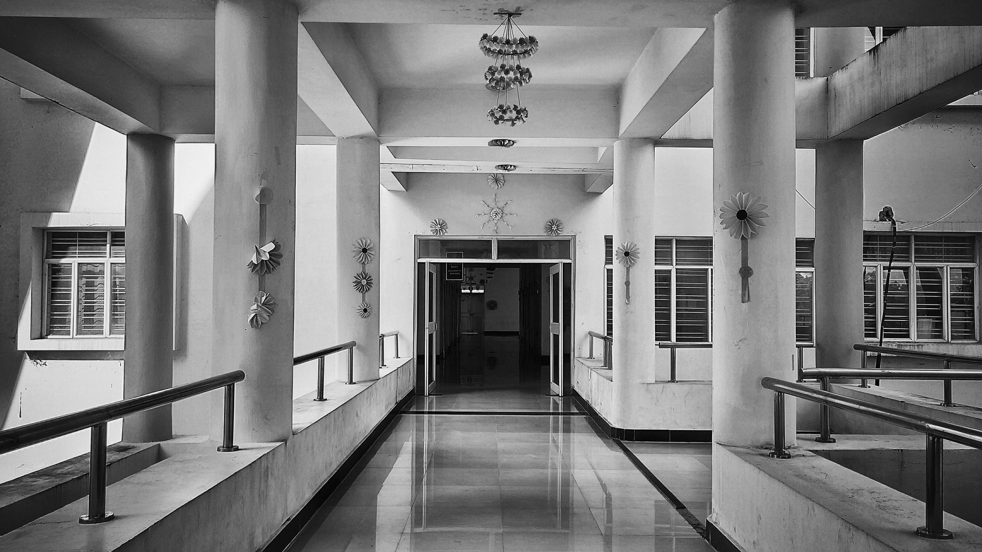 A long, white hallway with pillars and railings, leading to a door at the end.