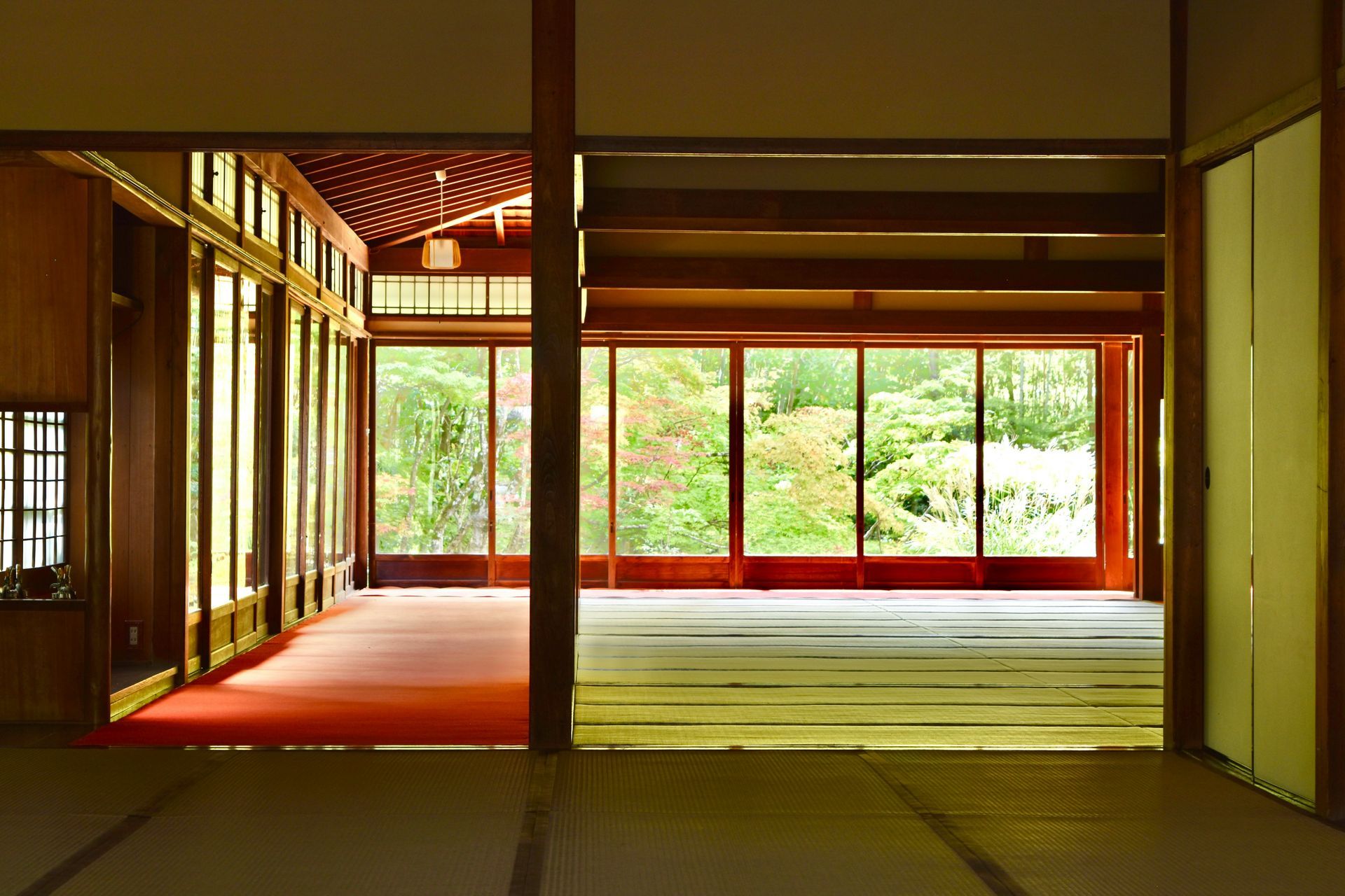 Japanese-style interior, rooms with sliding doors, overlooking a vibrant garden with red and green foliage.