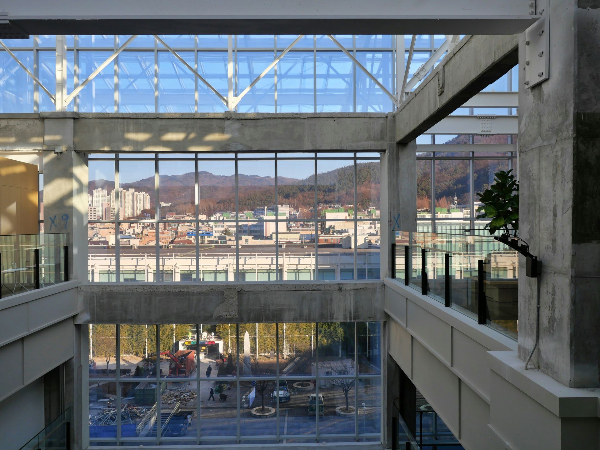 Indoor view with large windows overlooking a city with mountains; concrete and glass architecture.