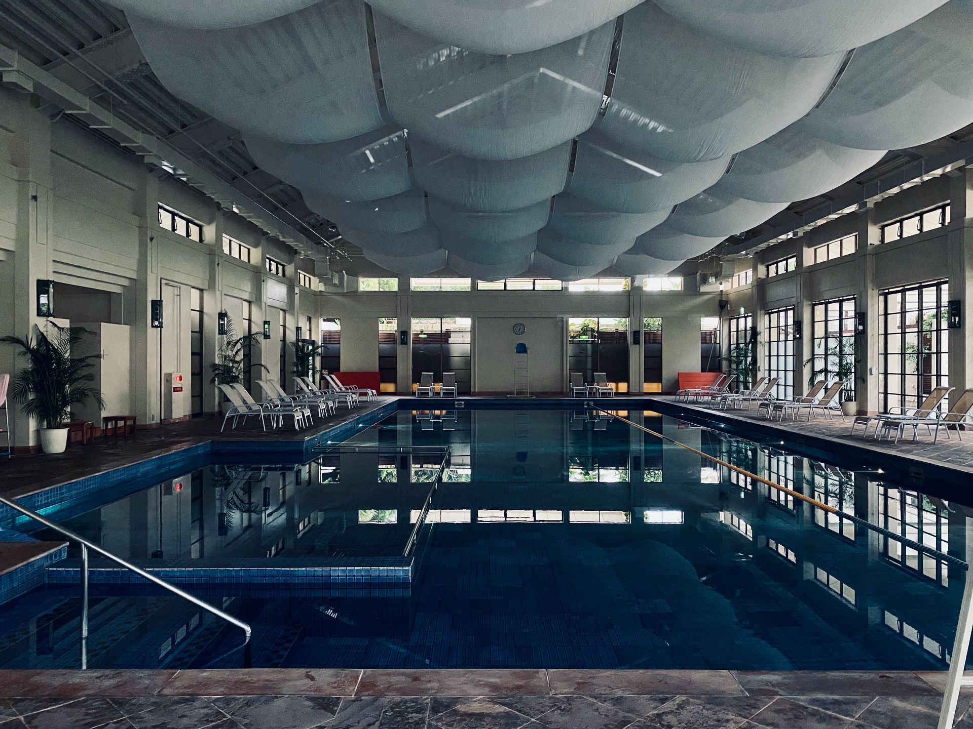 Indoor swimming pool with blue water, lounge chairs, and a unique cloud-like ceiling.