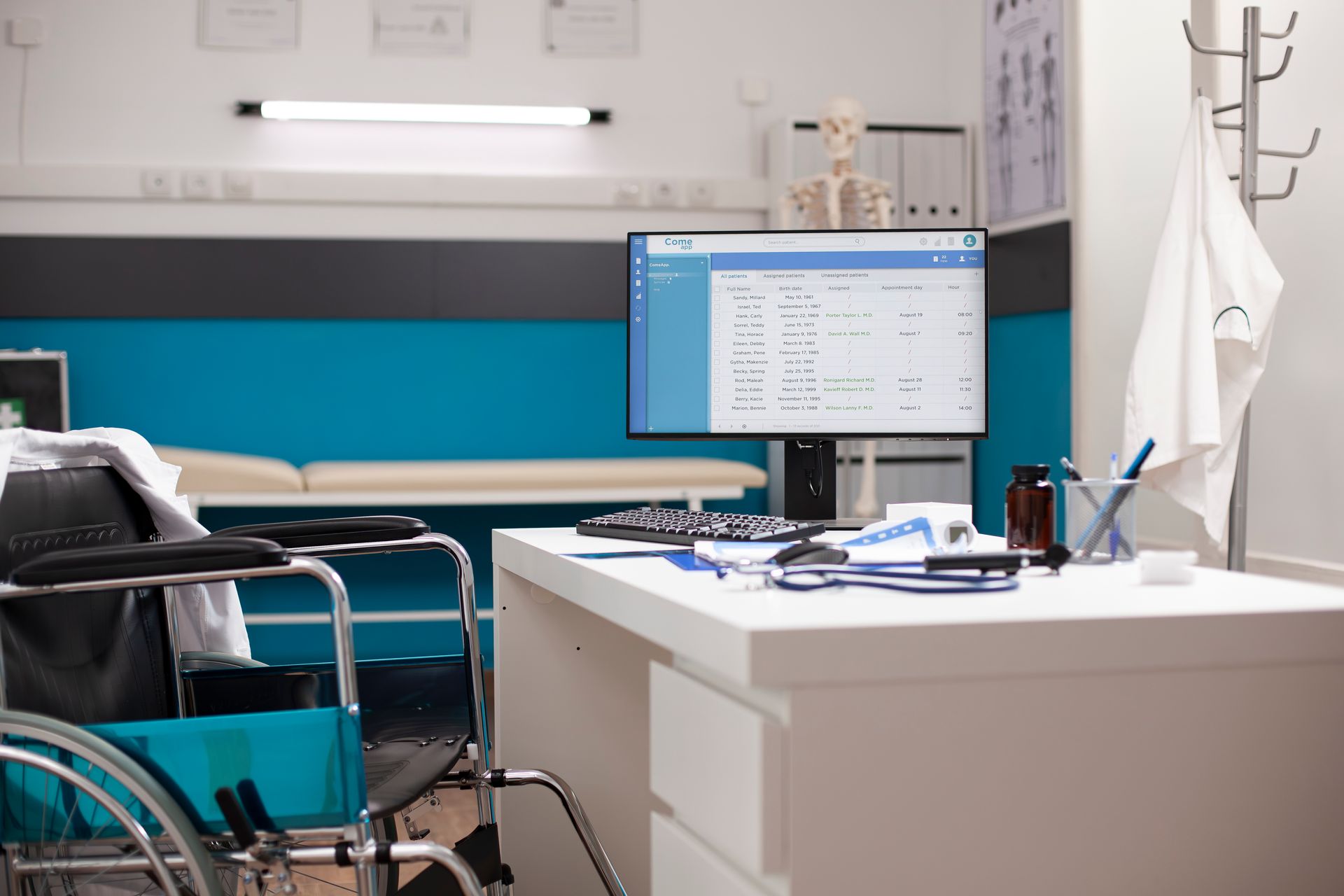 Doctor's office interior with a desk, computer, wheelchair, and examination table. Turquoise wall, white coat hanging.