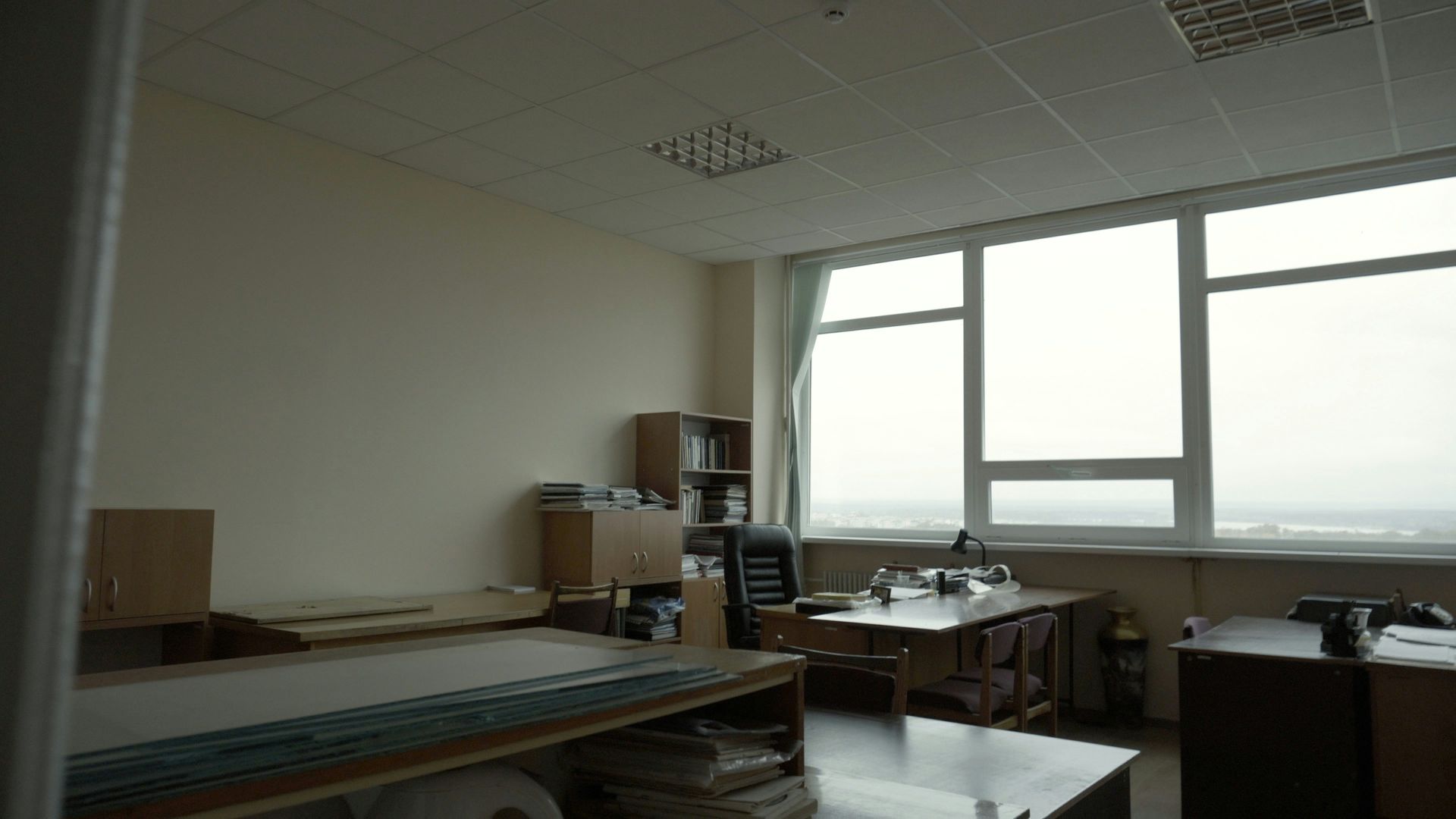 An office interior with a large window, desks, chairs, and shelves.