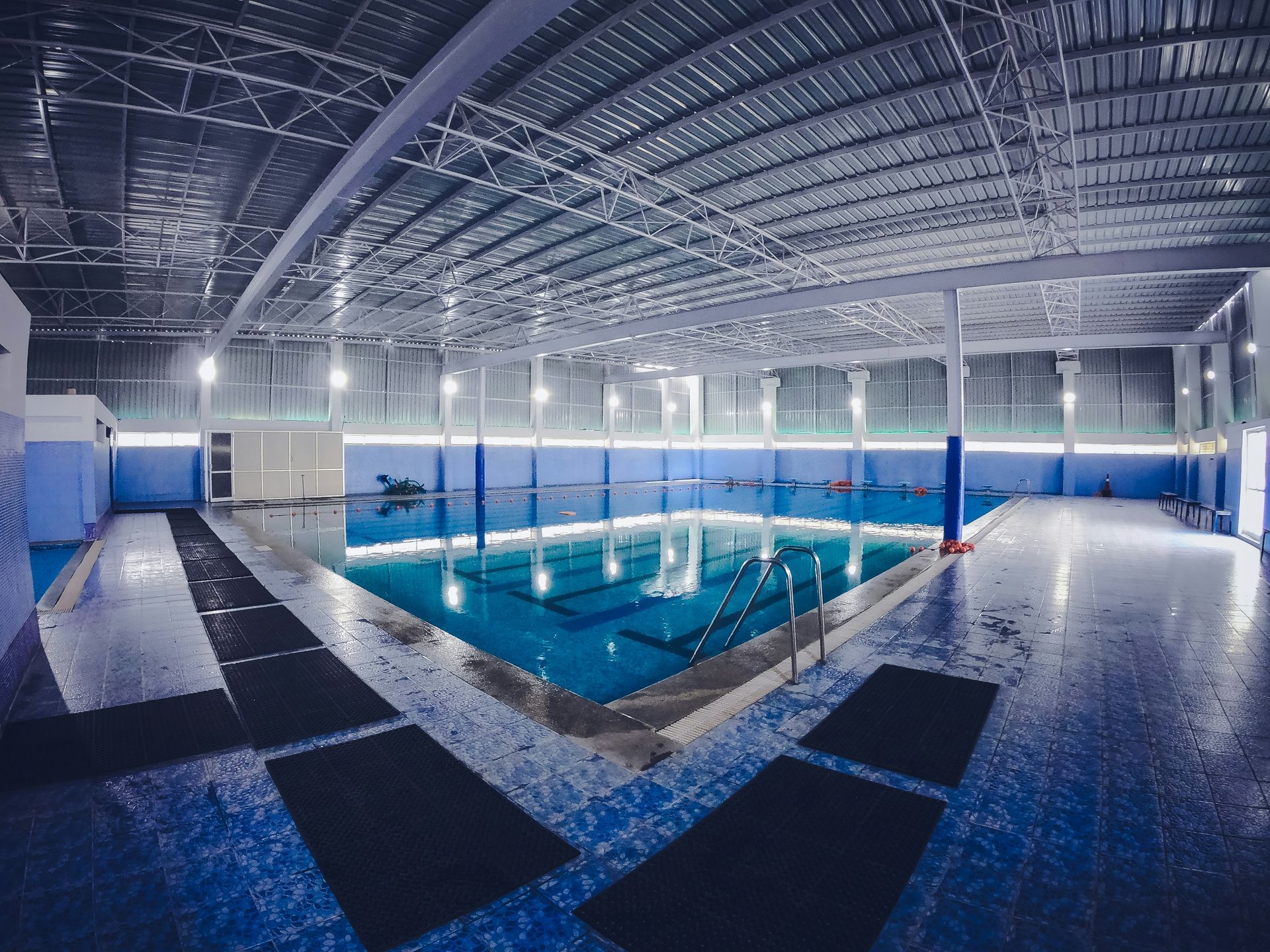 Indoor swimming pool, blue water, and floor. Blue walls, metal roof, no people.