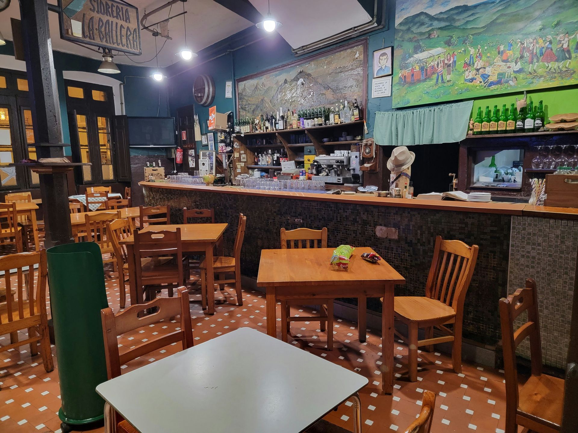 Interior of a rustic bar with wooden tables and chairs, bar counter, and art on the walls.