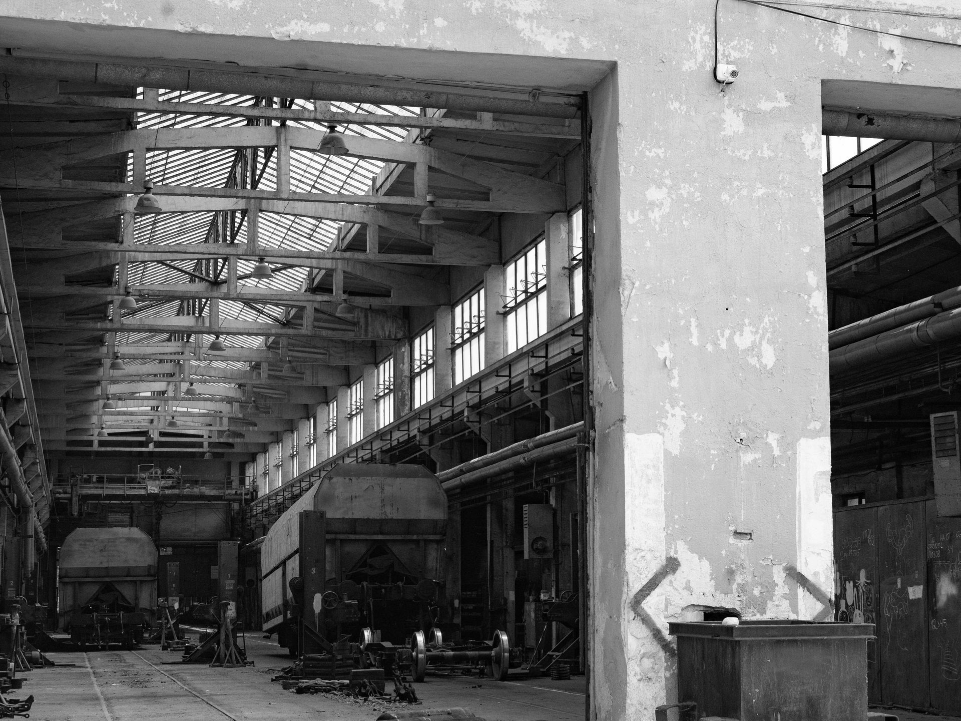 Inside a large, aged industrial building; train cars are in repair bays.
