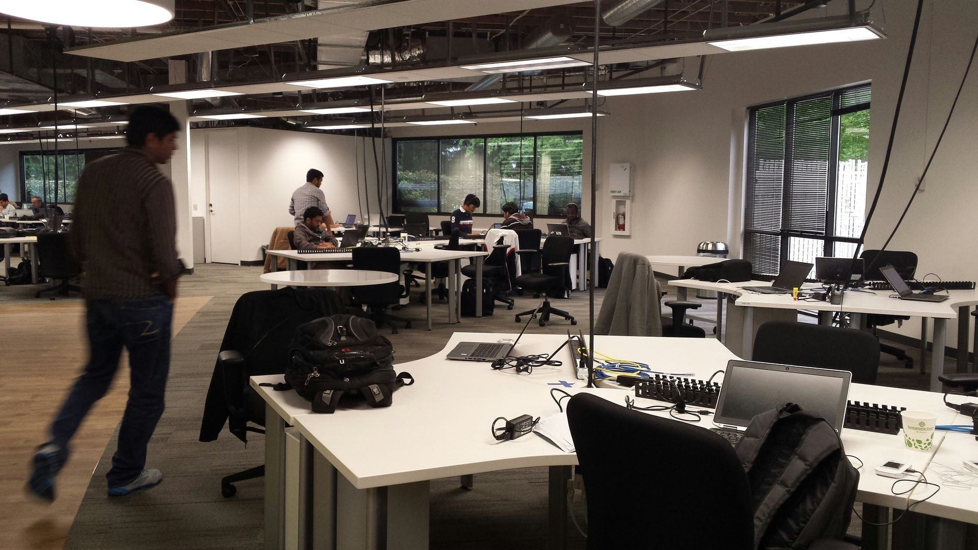 Two women at a table in a bright office. Grey sofa, round table, and big windows.