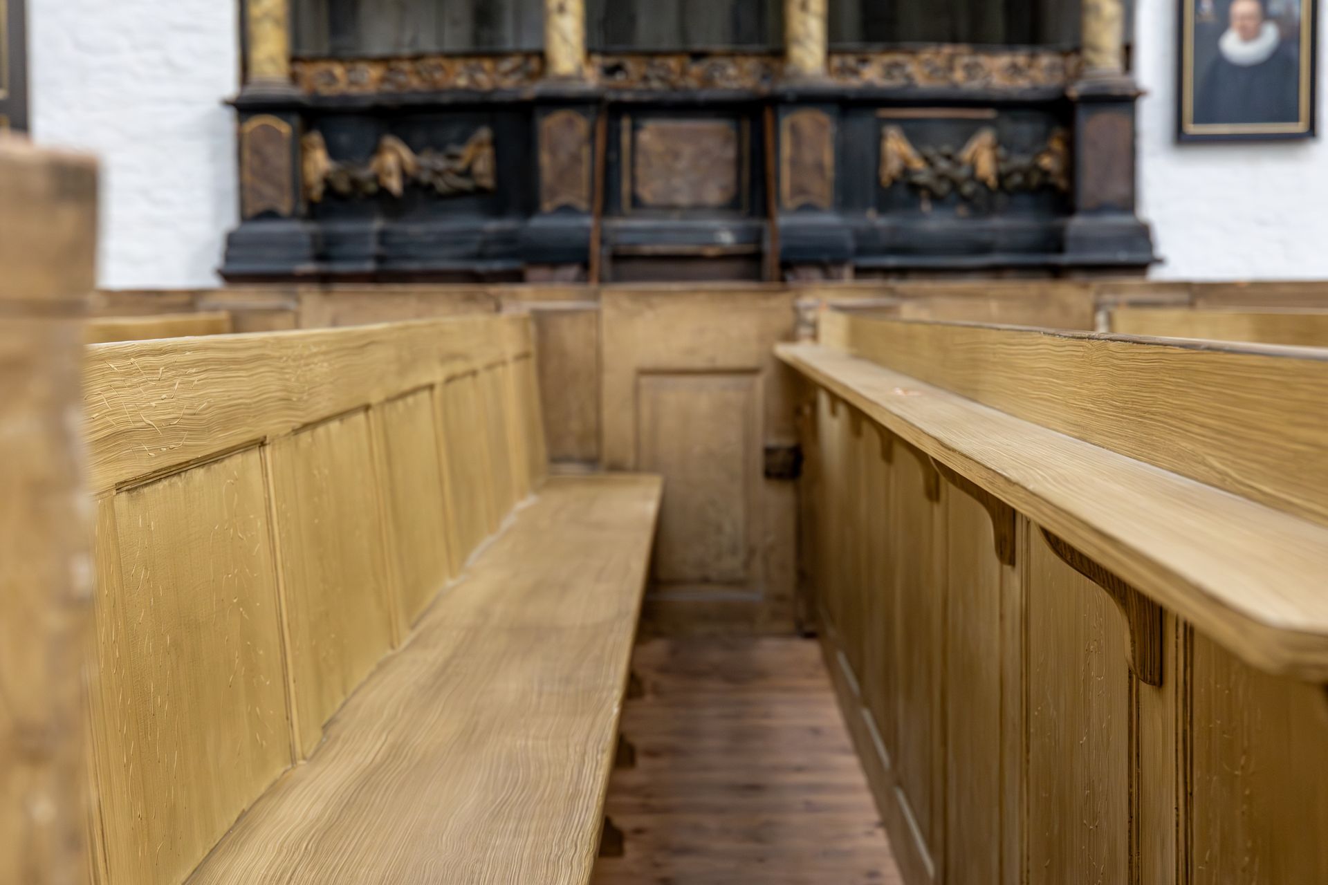 Wooden church pews, looking toward a decorative altar in a light-filled room.