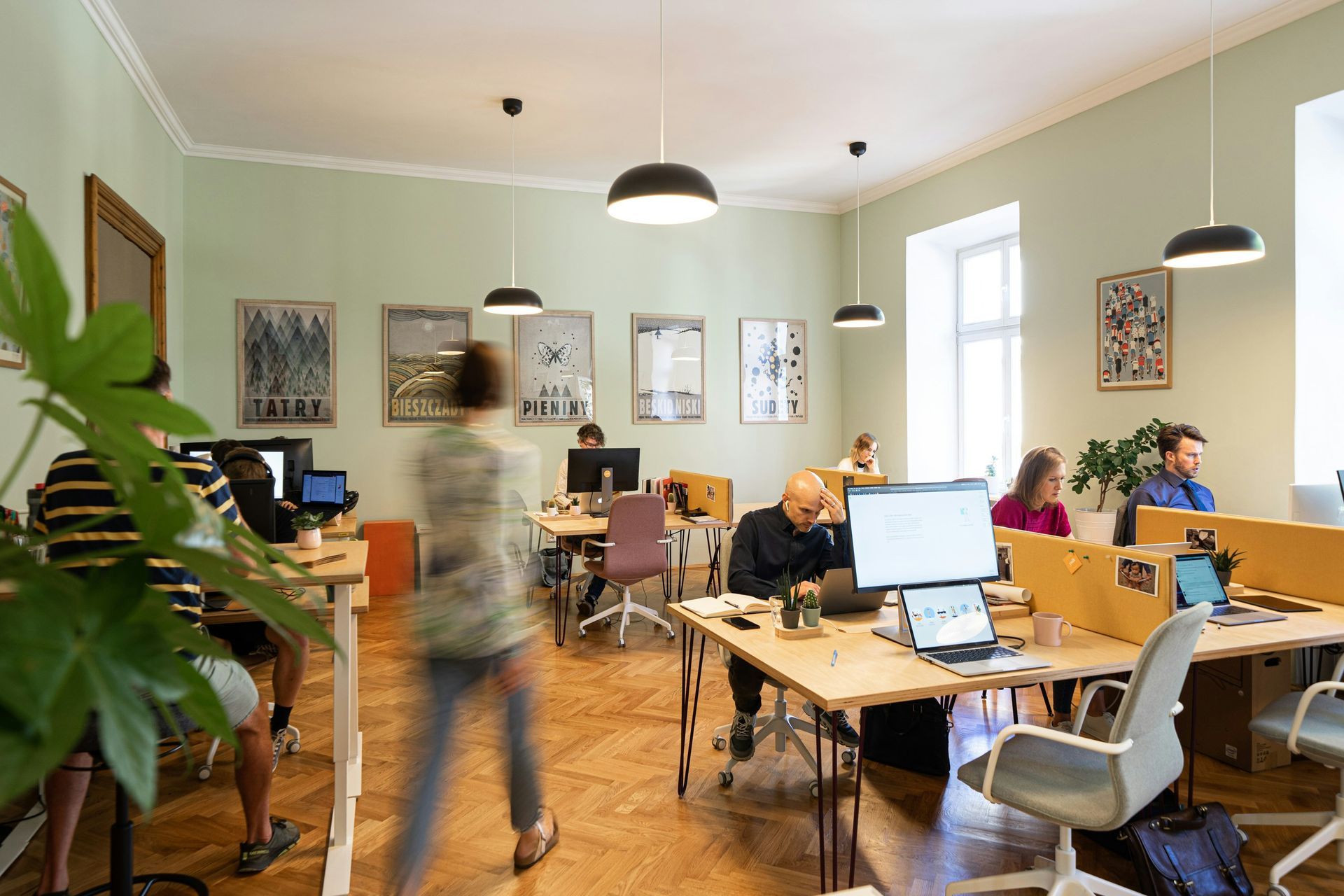 Office with people working at desks, light green walls, wood floors, and artwork.