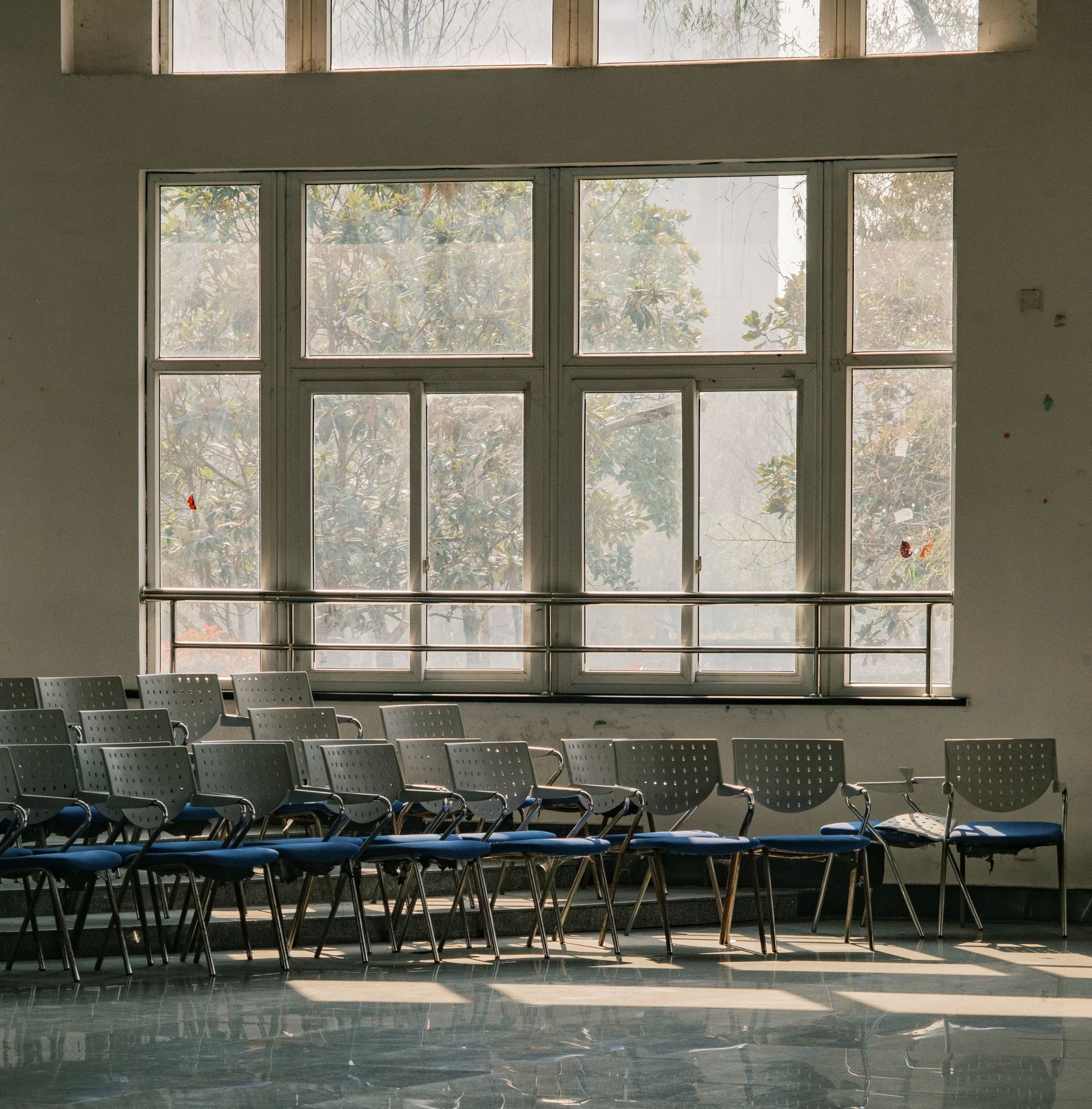 Rows of blue chairs face a large window in a sunlit classroom.