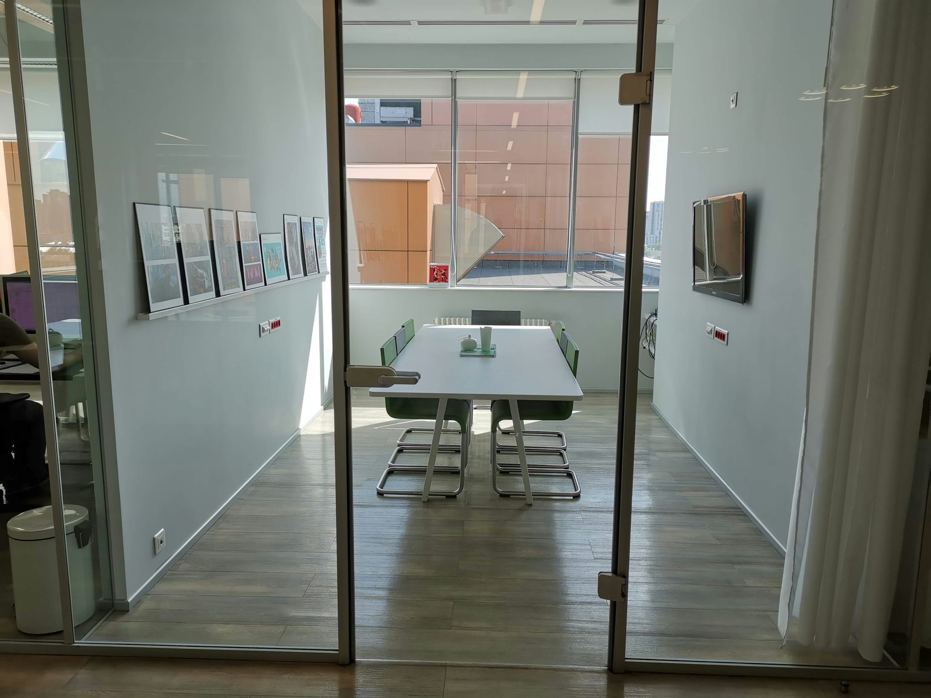 Glass-walled conference room with a white table, green chairs, and natural light.