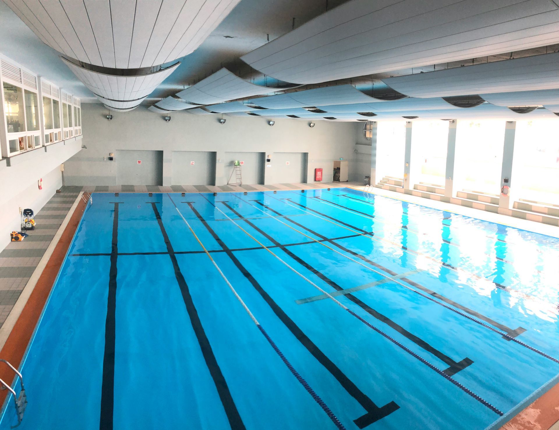 An indoor swimming pool with lanes marked by black lines; blue water and surrounding white walls.