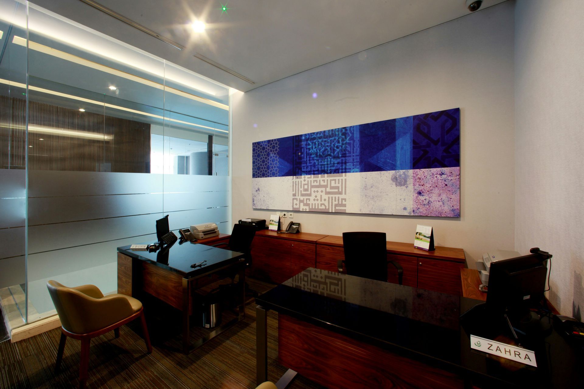 Modern office with two desks, a large blue abstract painting, and frosted glass.