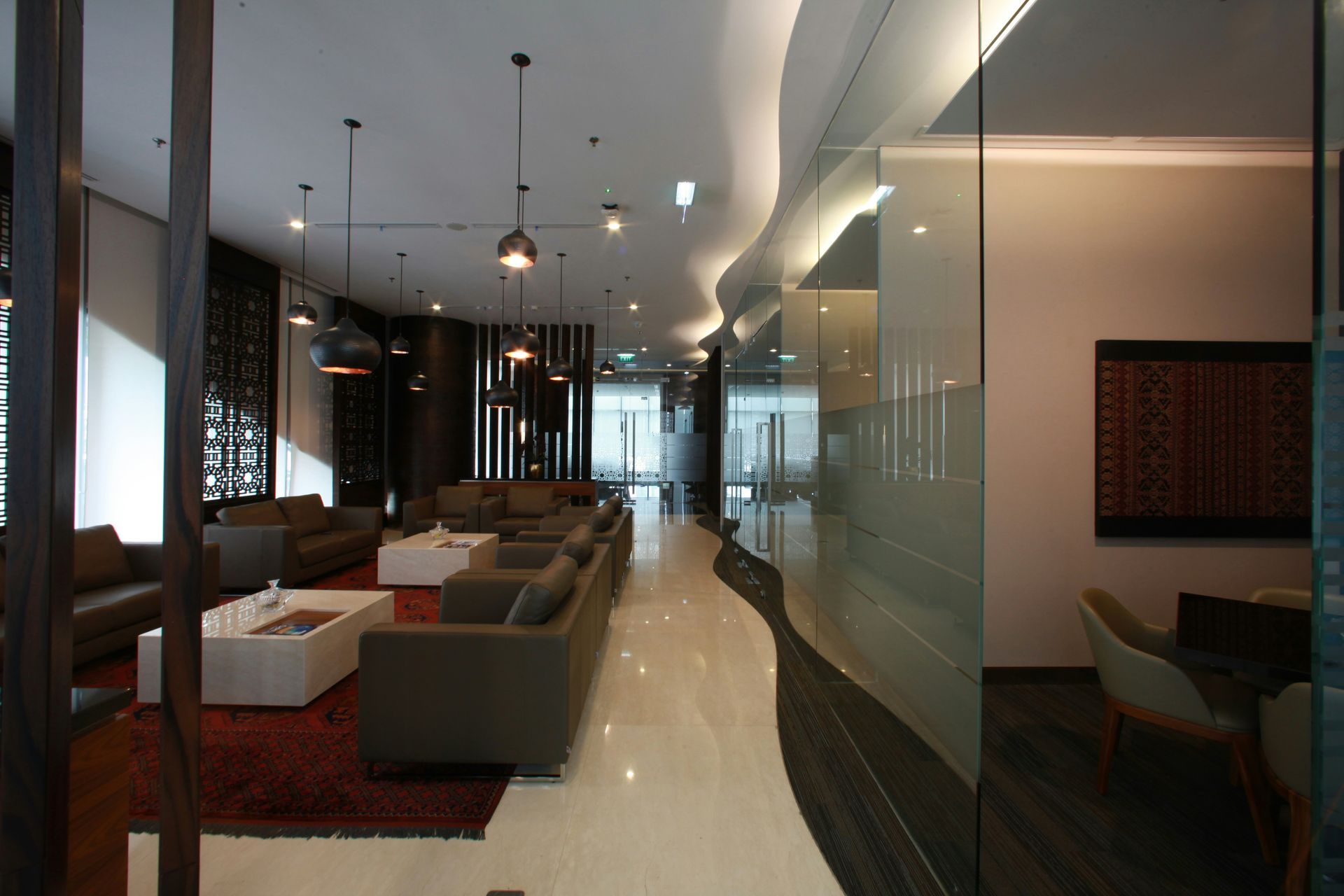 Lounge area with couches, low tables, and decorative lighting. Glass walls and dark wood accents.