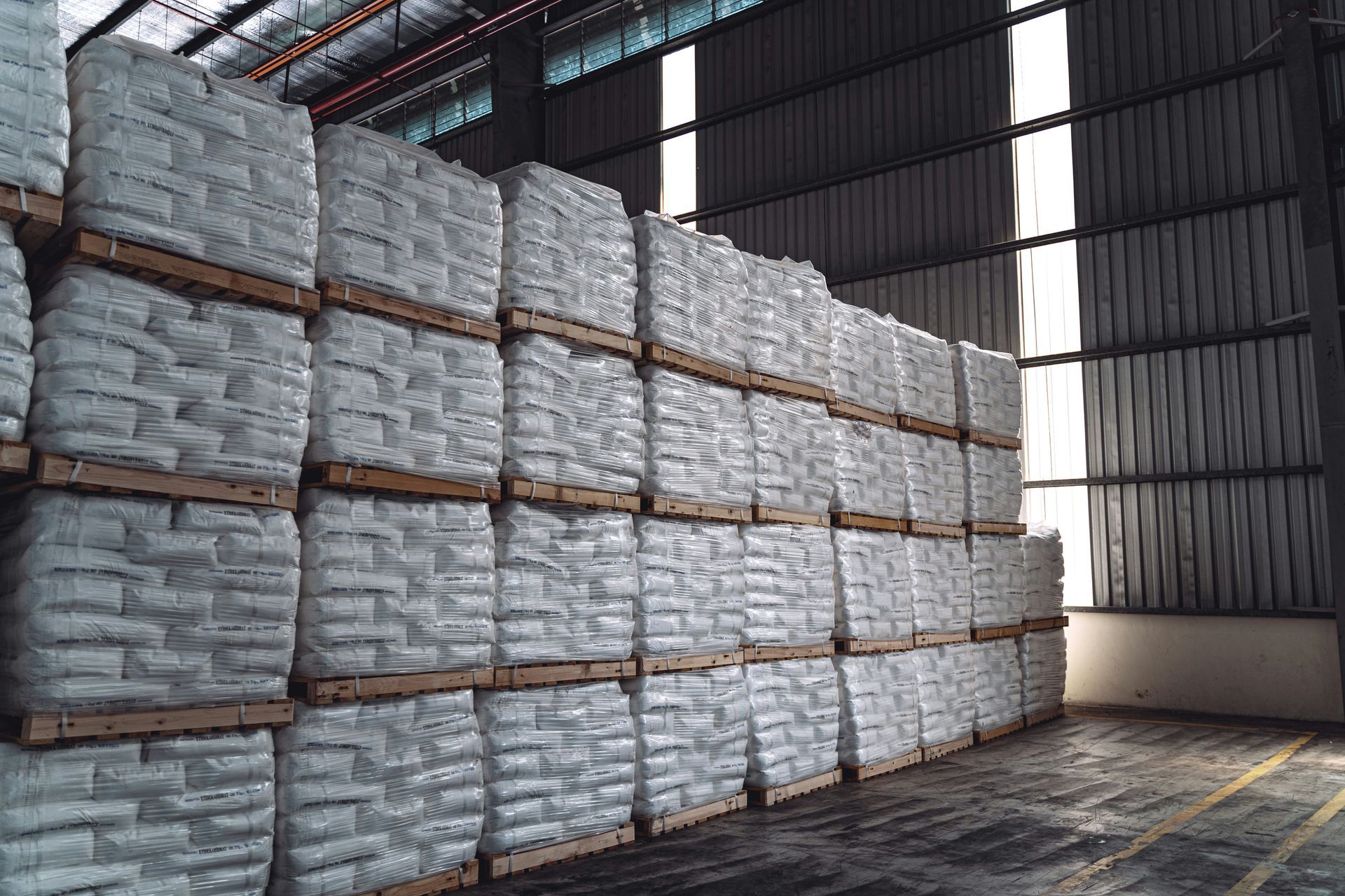 Large warehouse filled with stacked pallets of white bags.