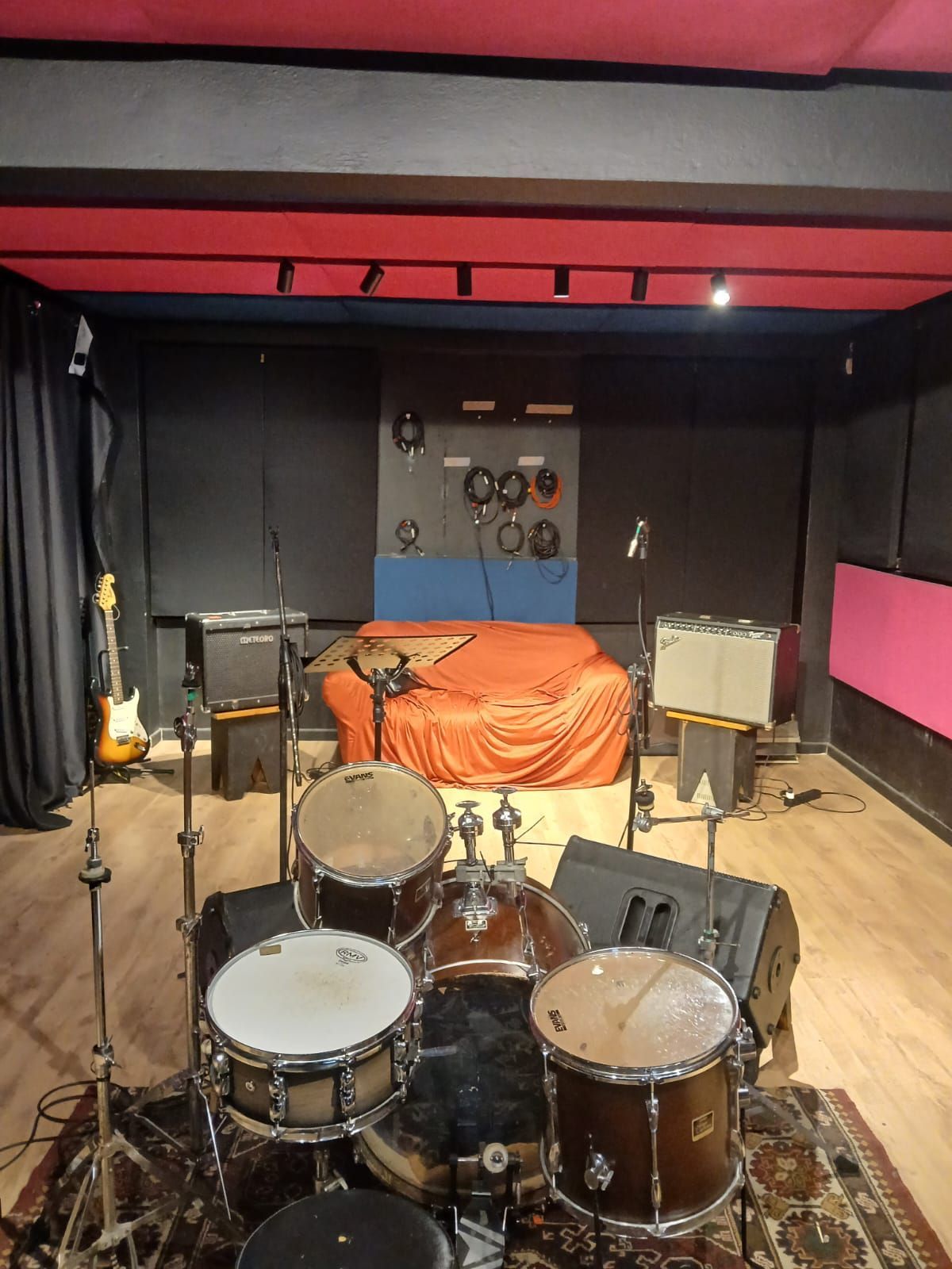 Uma bateria está em uma sala com uma cama ao fundo.