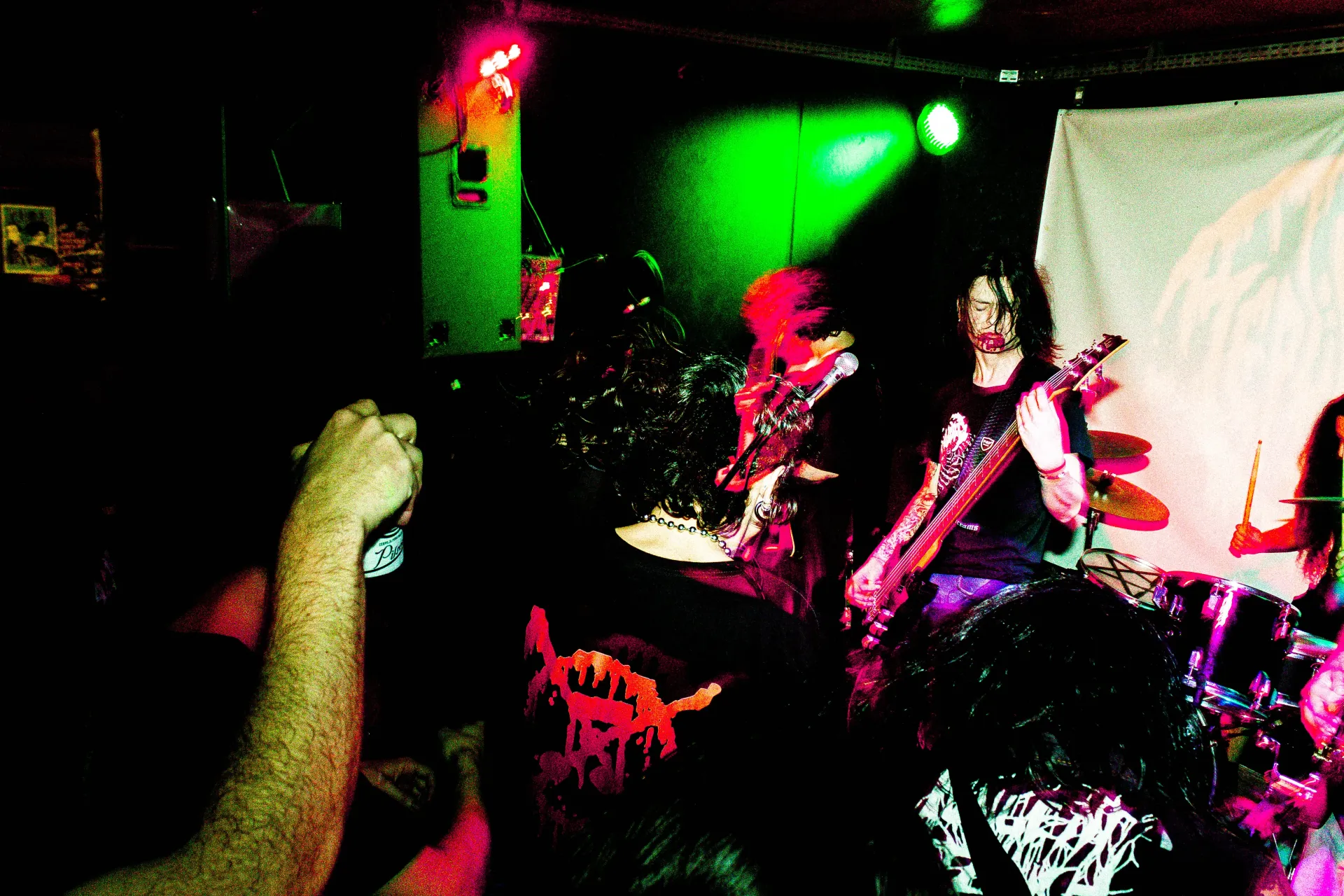 Um grupo de pessoas está em uma sala escura assistindo a uma banda se apresentar no palco.