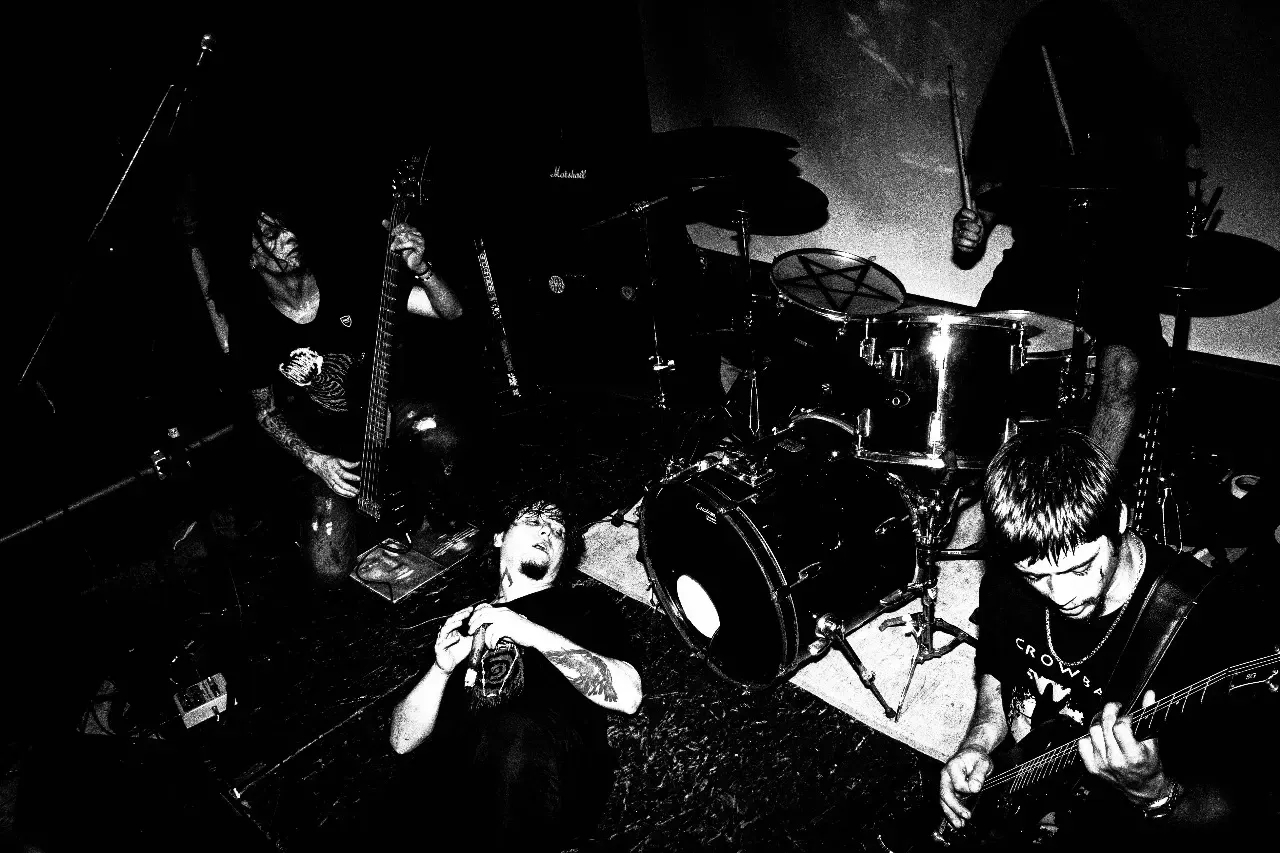Show da banda Sepulcro. Vocalista deitado no palco com microfone, guitarrista e baterista tocando em ambiente escuro.