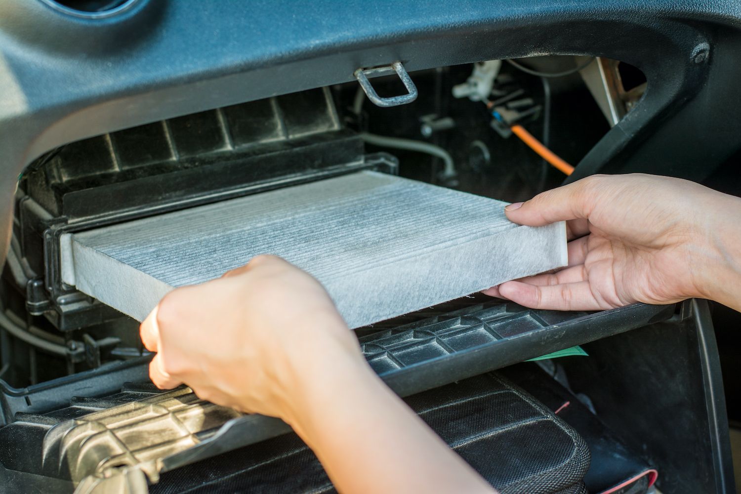 Hands replacing a dusty cabin air filter in a car's dashboard compartment.