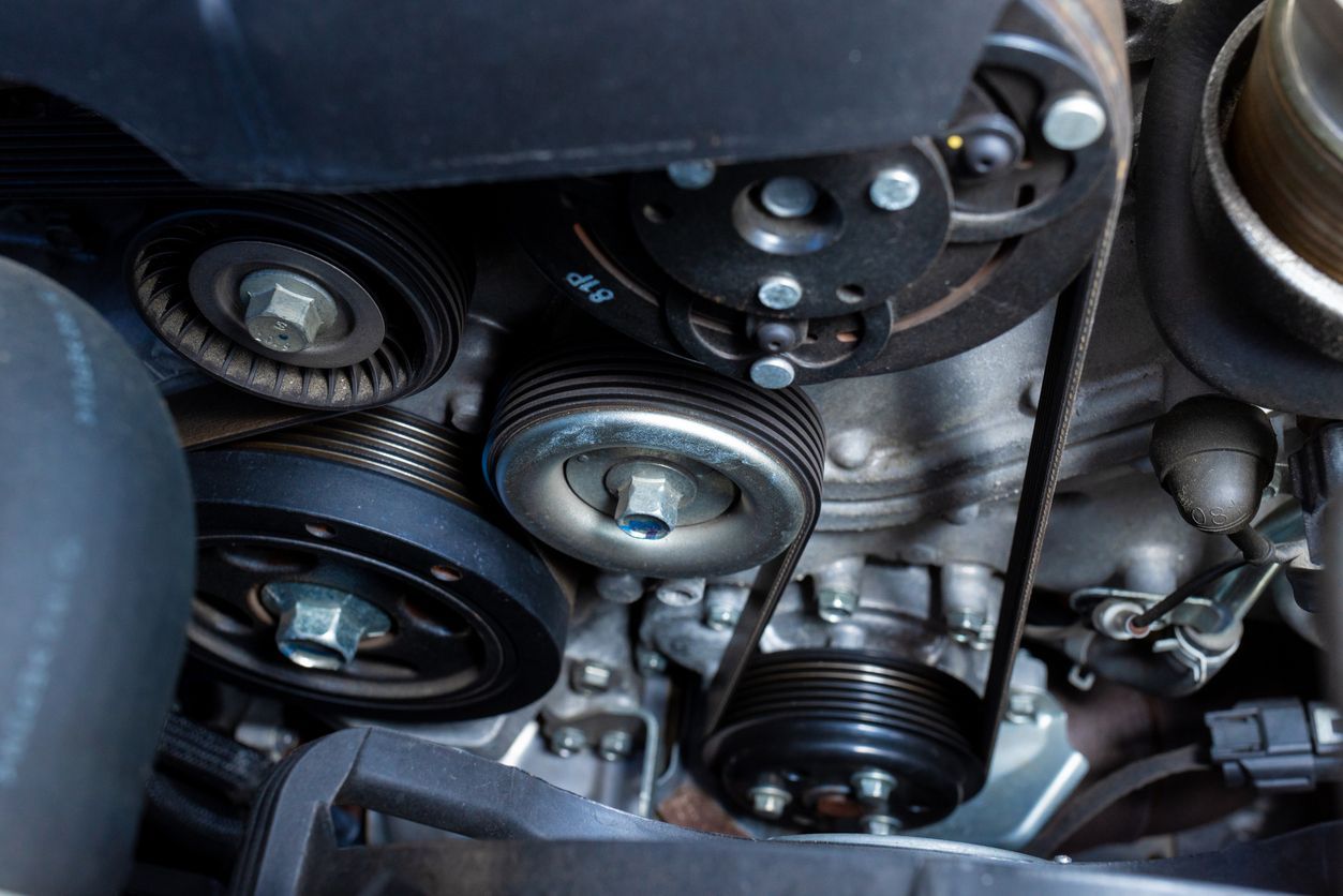 Close-up of a car engine's serpentine belt wrapped around various pulleys and components.