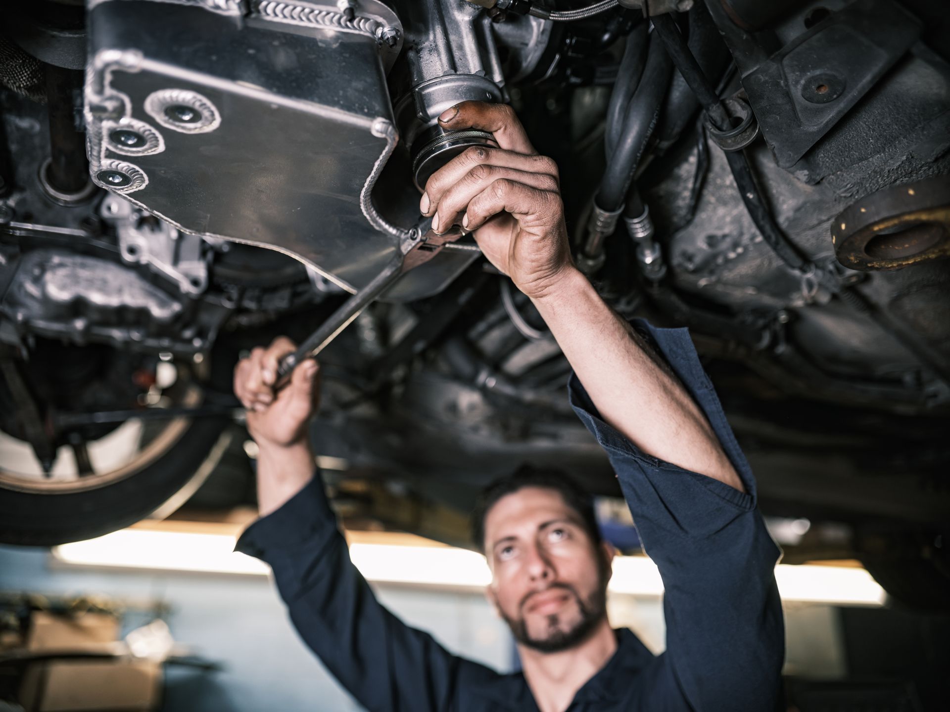 Mechanic working under a car, holding a wrench, focused, in a garage.