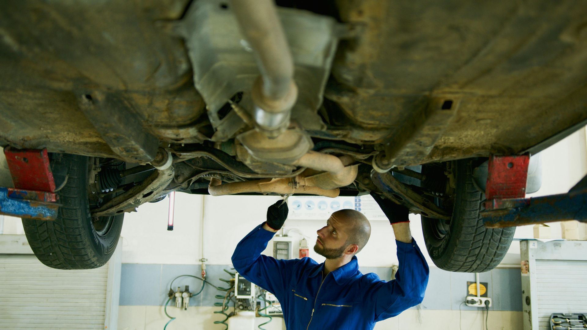 Mechanic in blue jumpsuit works under a car lifted on a hoist.