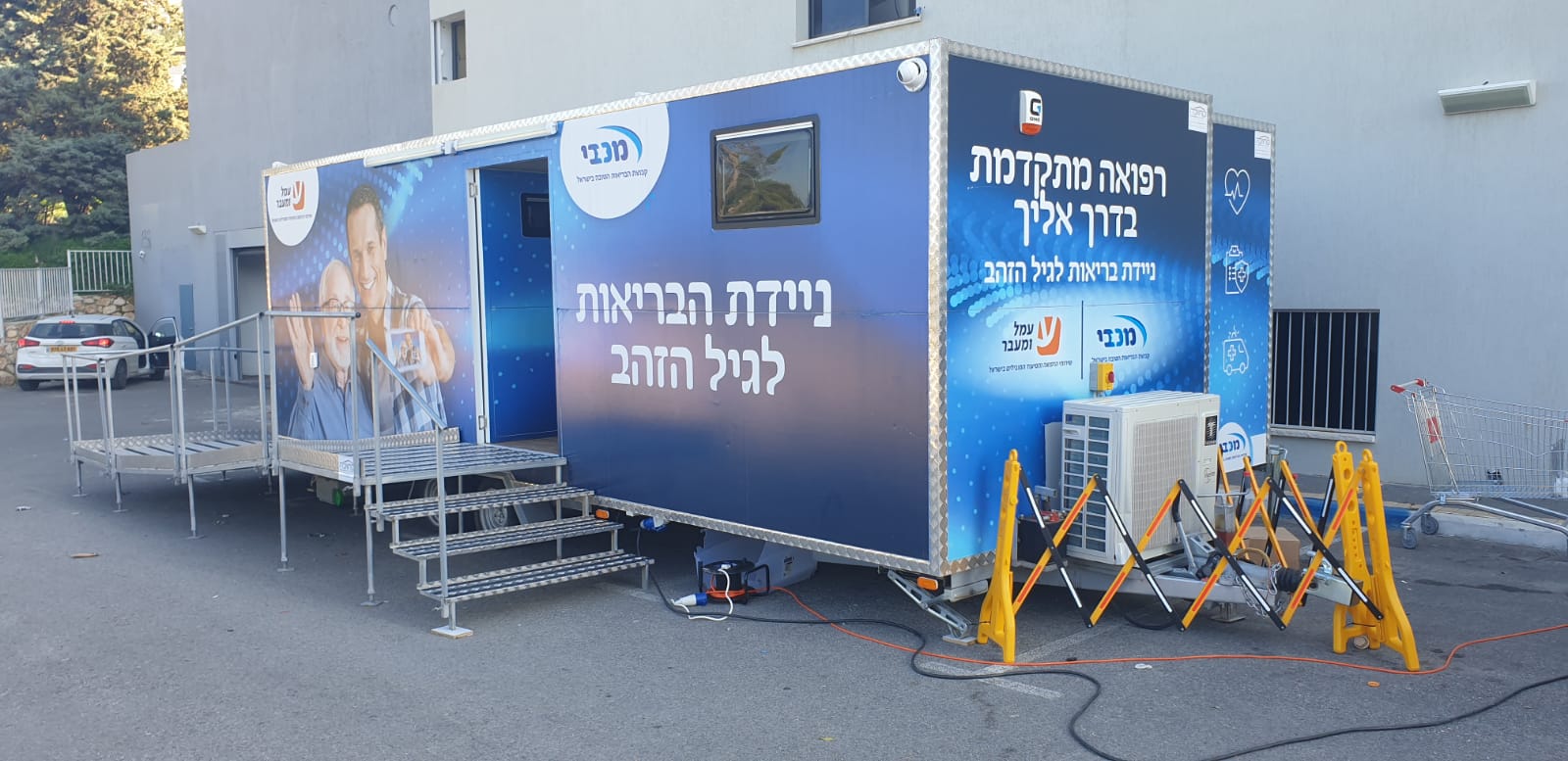 קרוואן כחול עם כיתוב בעברית חונה מול בניין.