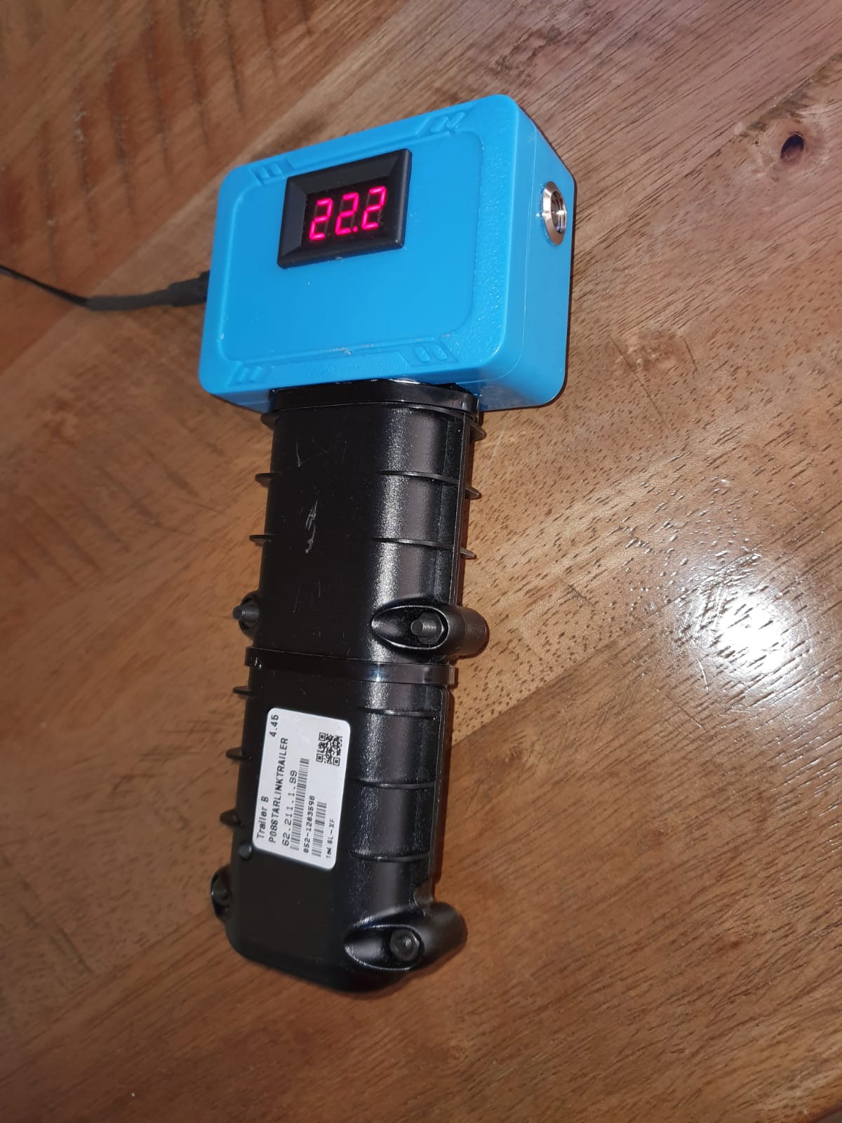 קופסה כחולה עם צג דיגיטלי עליה מונחת על שולחן עץ.