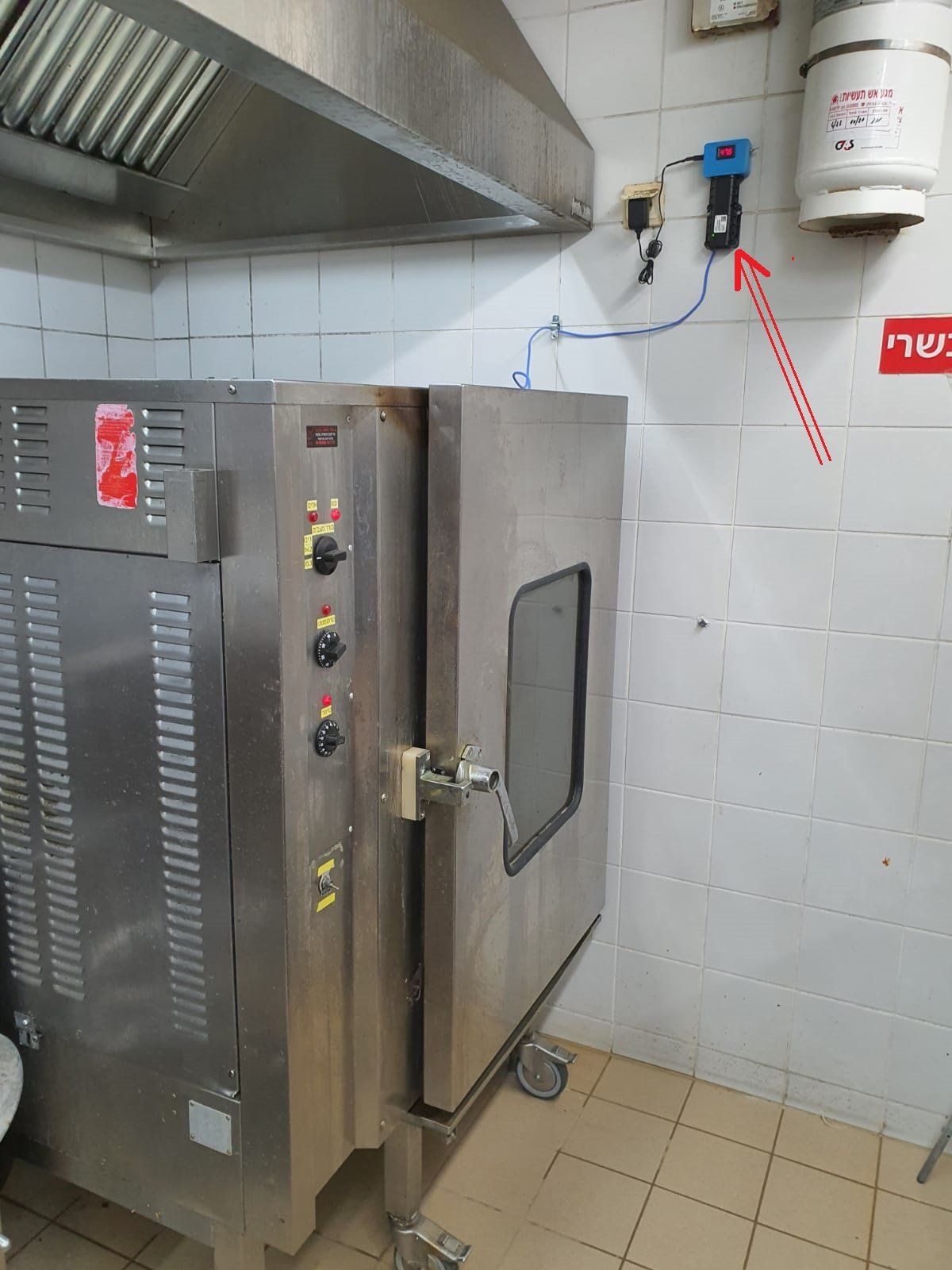 תנור נירוסטה מונח במטבח ליד מטף כיבוי אש.