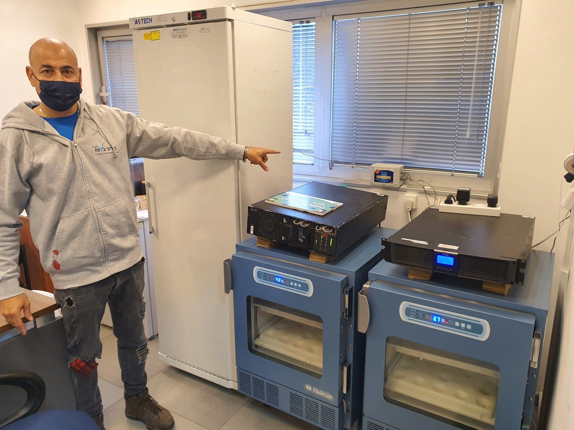 גבר חובש מסכה מצביע על מקרר בחדר.