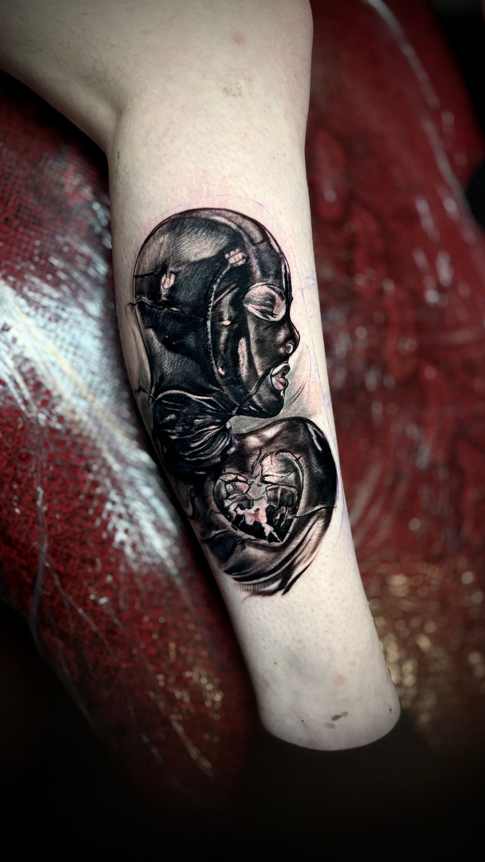 Black and gray tattoo of a fetus inside the womb on an arm.