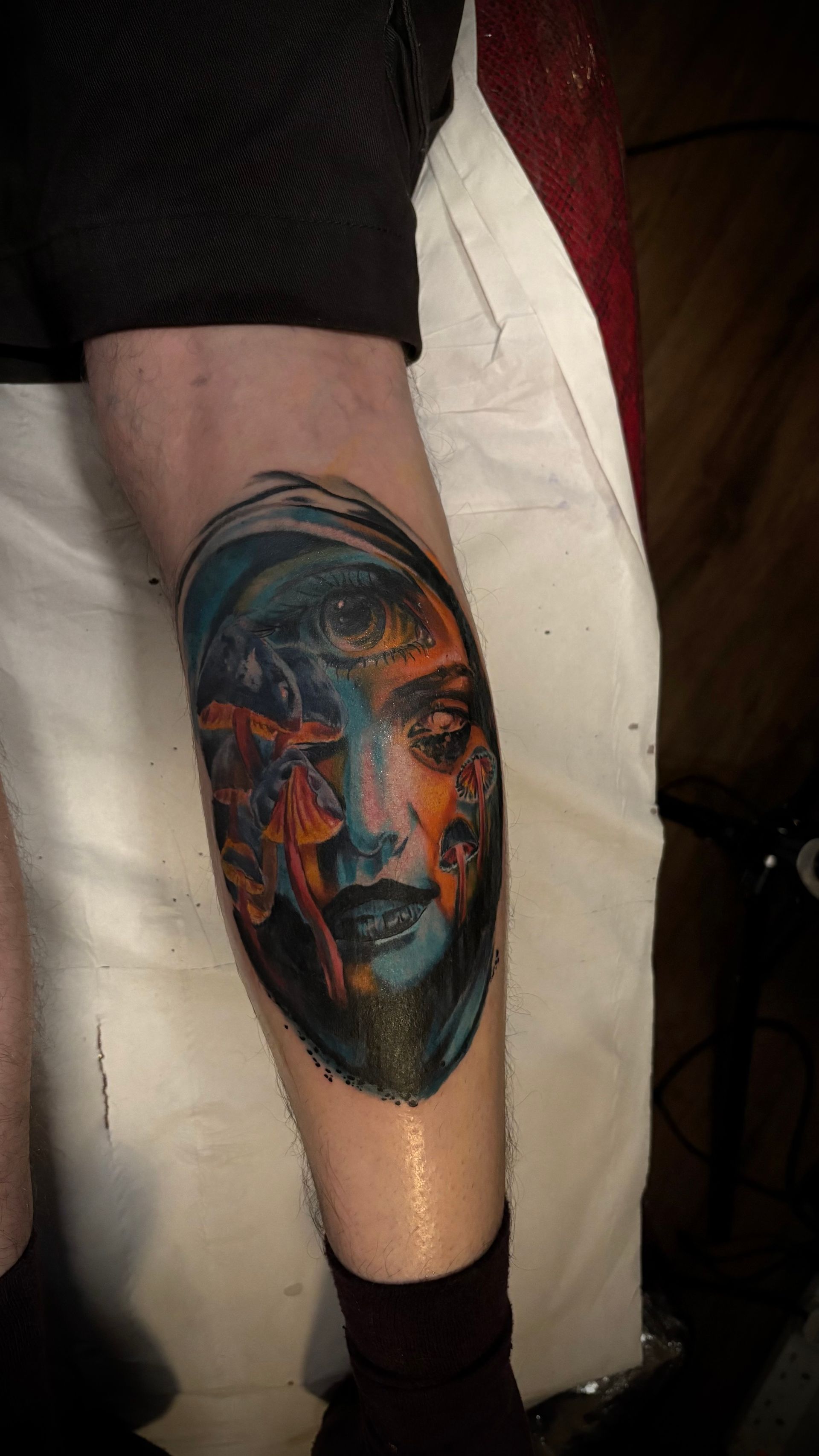 Tattoo of a face on a leg. The face is divided with orange and blue colors. The skin is wet.