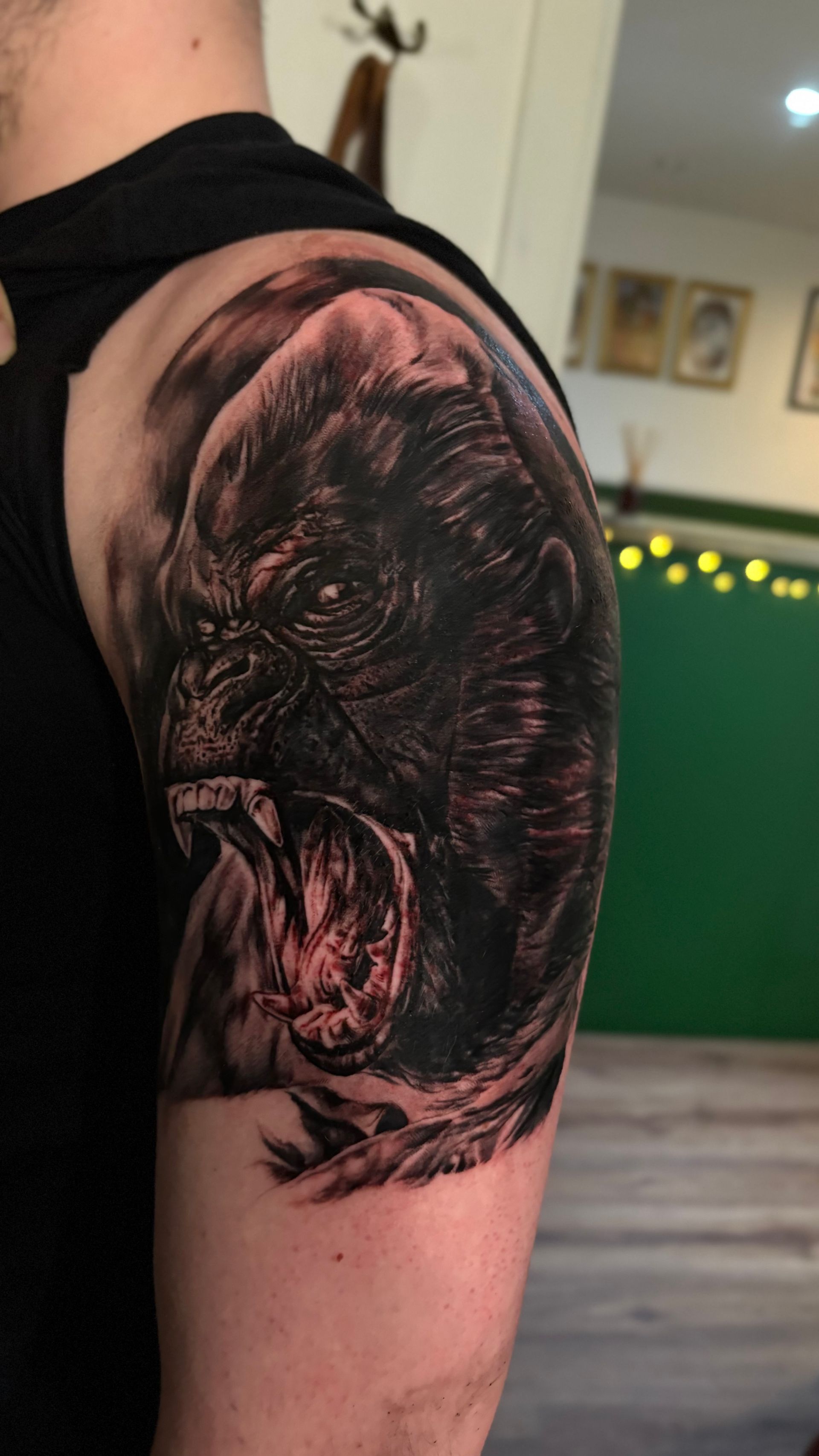 Detailed gorilla tattoo on a person's upper arm, with open mouth, dark colors, and visible teeth.