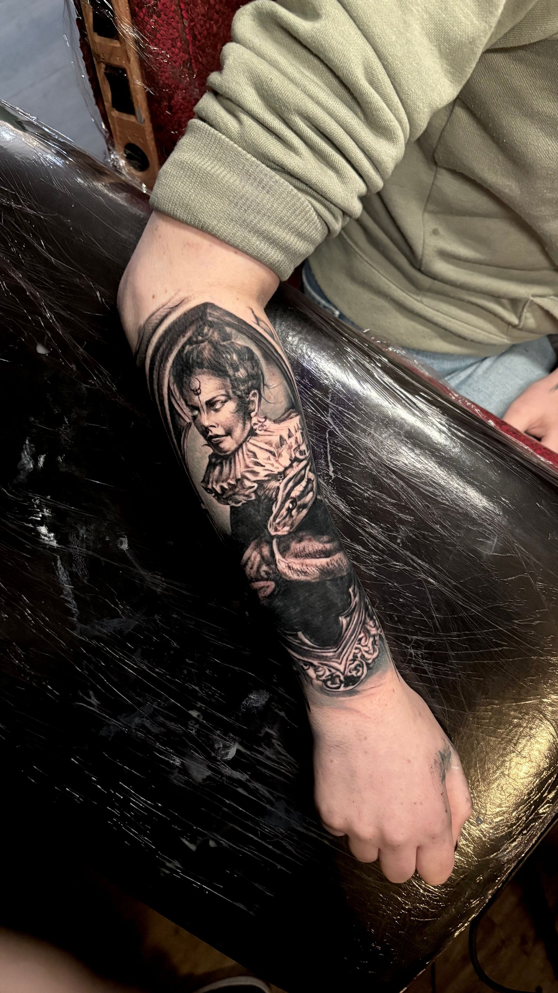Tattoo on an arm. Portrait of a woman with ornate clothing, black and gray. Arm resting on a black surface.