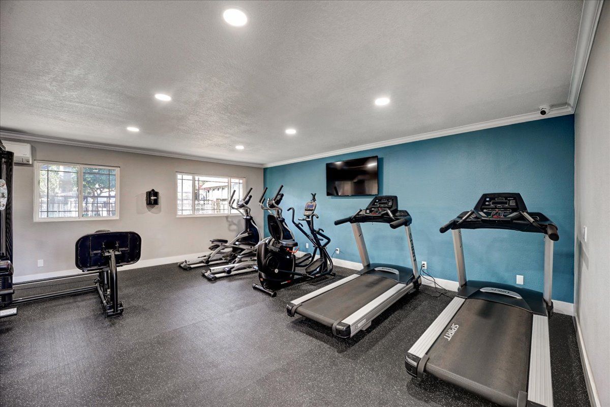 A gym with treadmills , bikes , and a television on the wall.