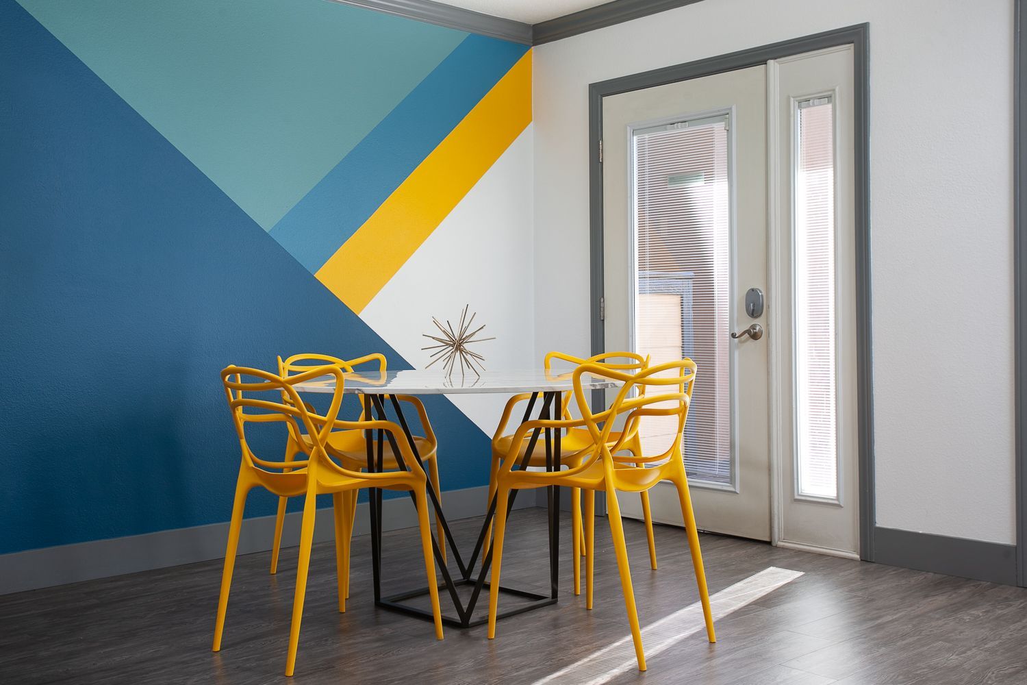 A room with a table and chairs in front of a colorful wall.