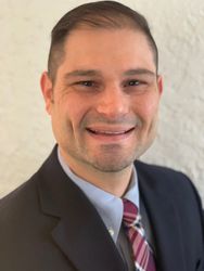Agent Denny in a suit and tie is smiling for the camera.