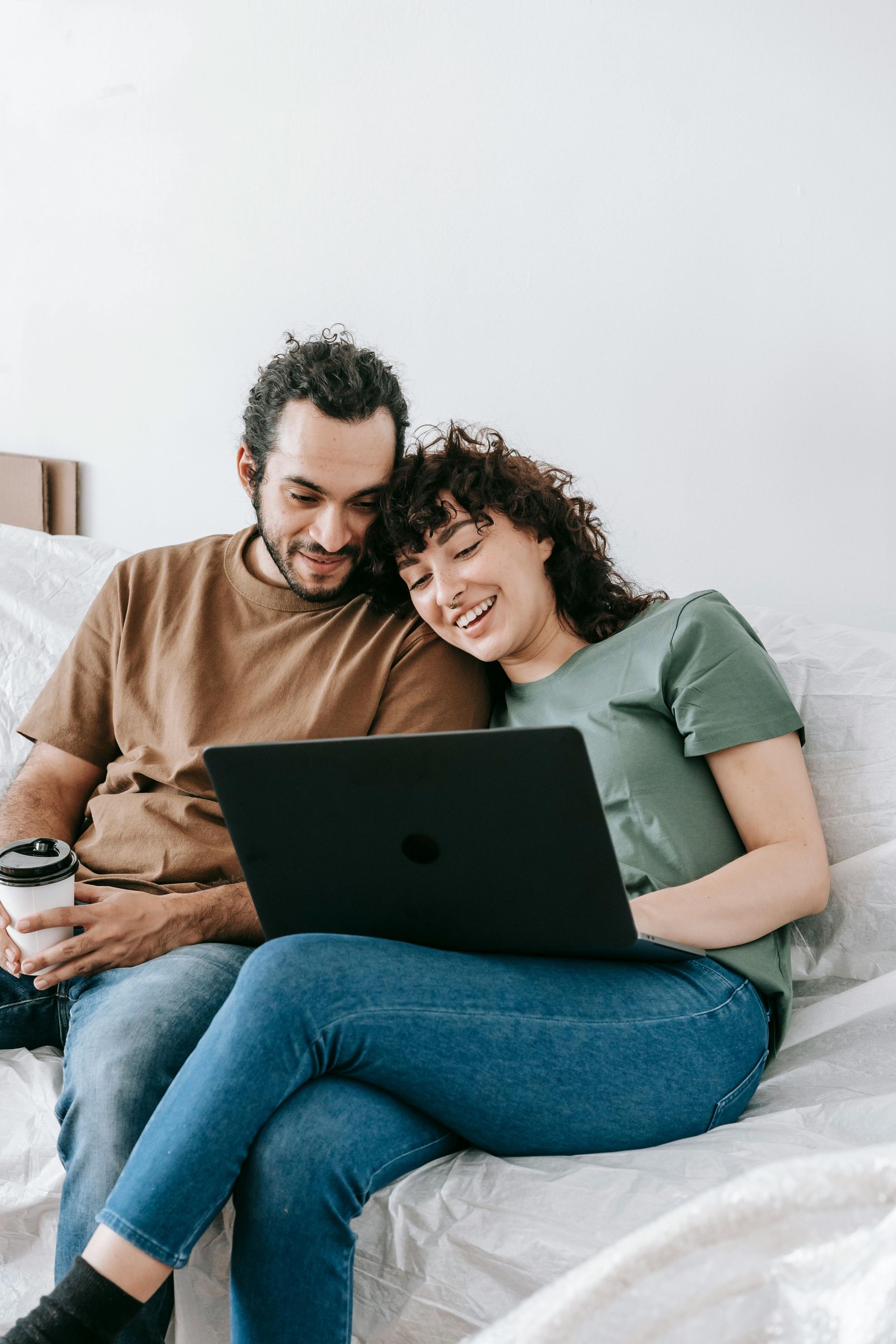 A man and a woman are sitting on a bed looking at a laptop.
