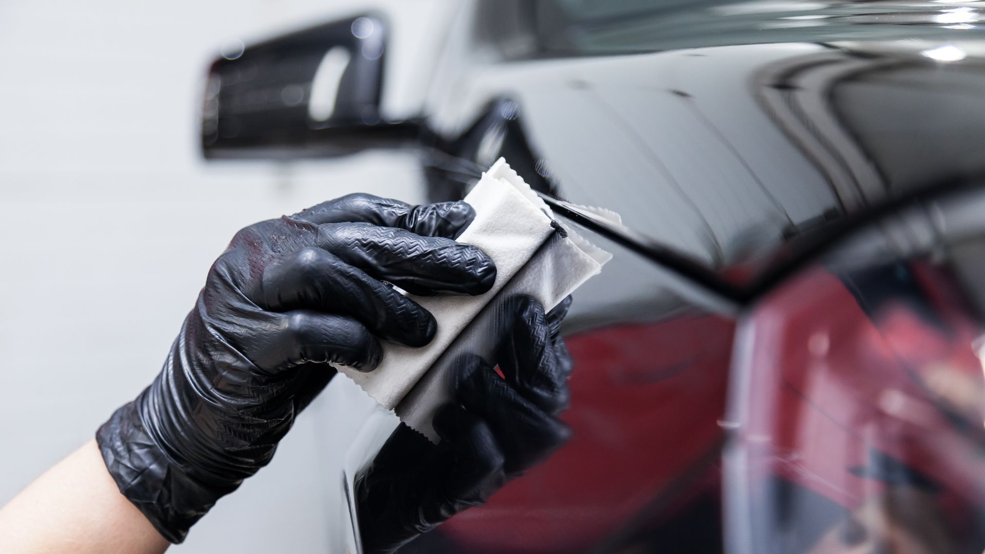 A person wearing black gloves is polishing a black car.