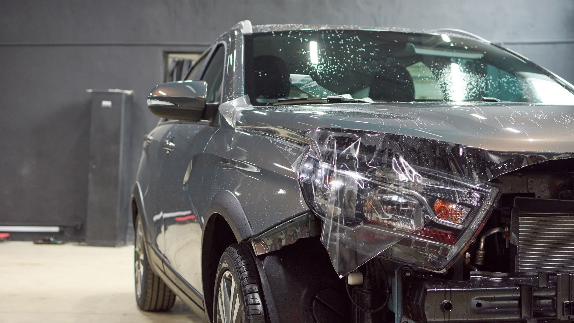 A car is covered in plastic wrap in a garage.