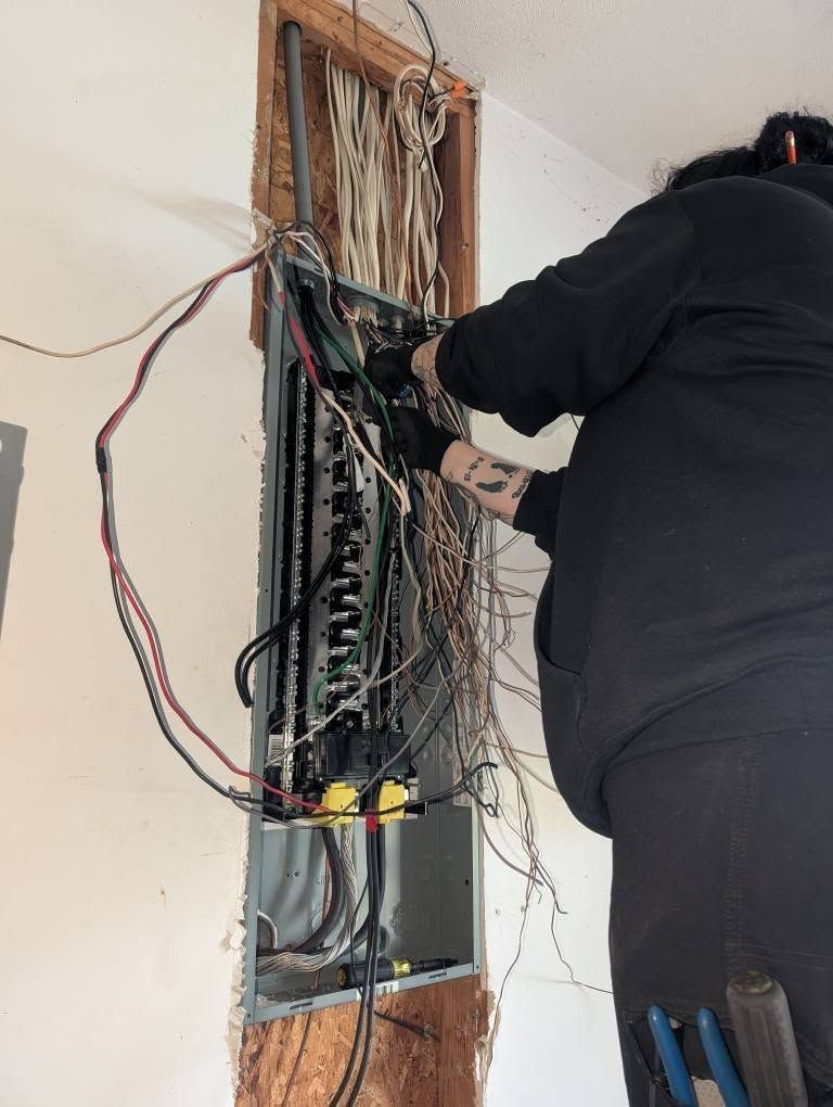 A man is working on an electrical box on a wall.